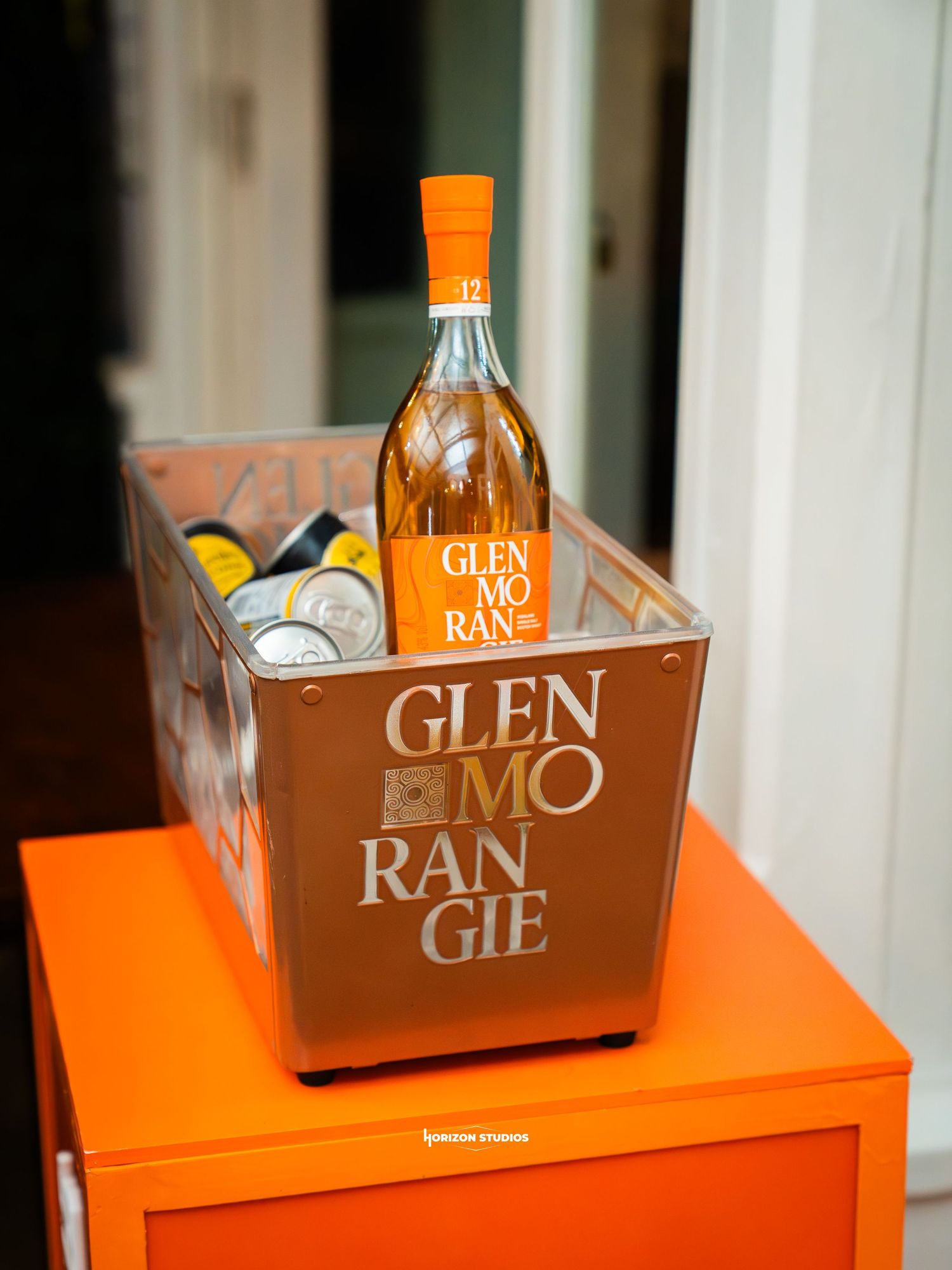 Glenmorangie 12 year Scotch whisky bottle displayed in branded orange ice bucket on matching orange cabinet.
