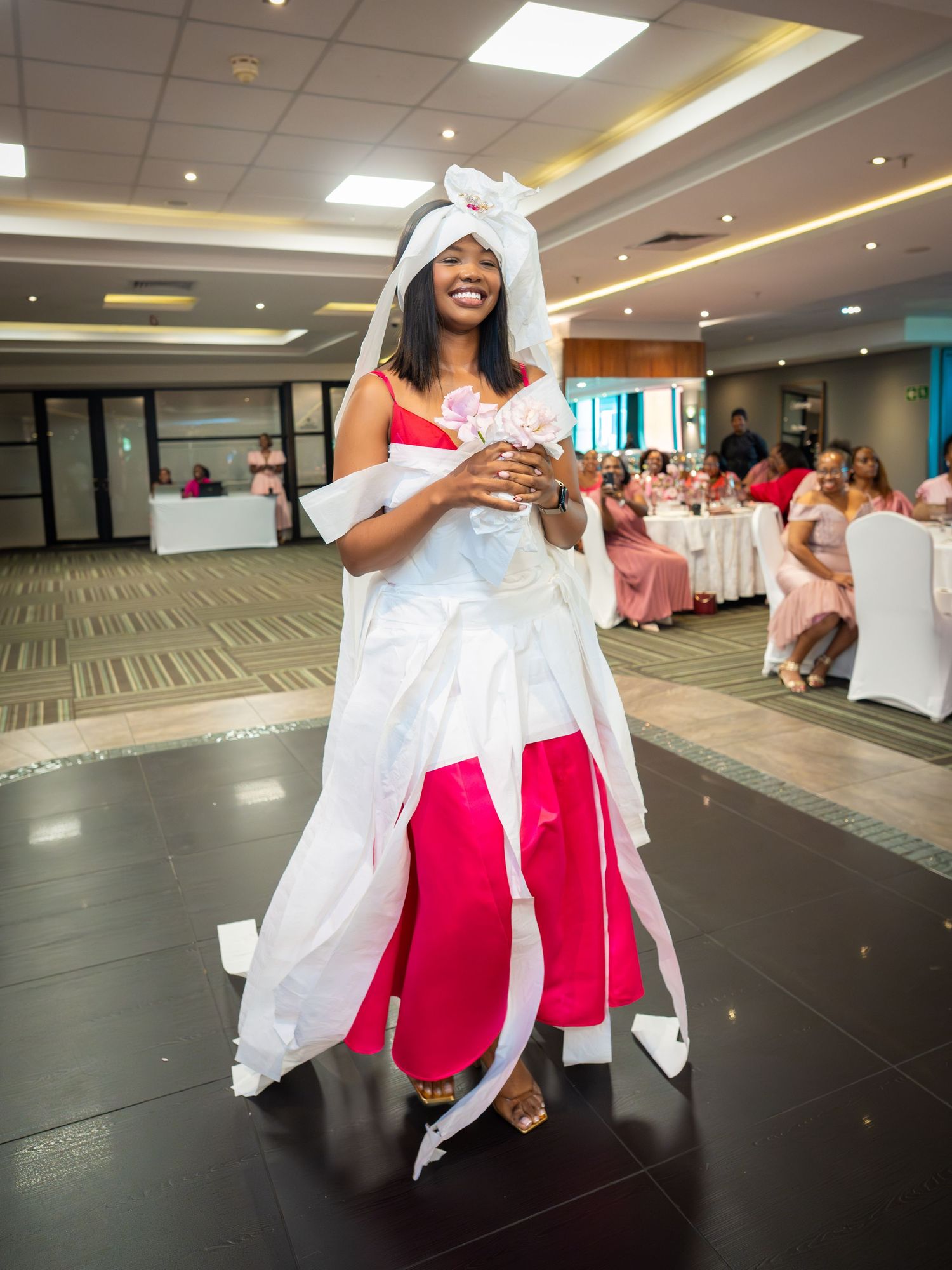 Woman in white and pink traditional dress smiling at indoor celebration event.