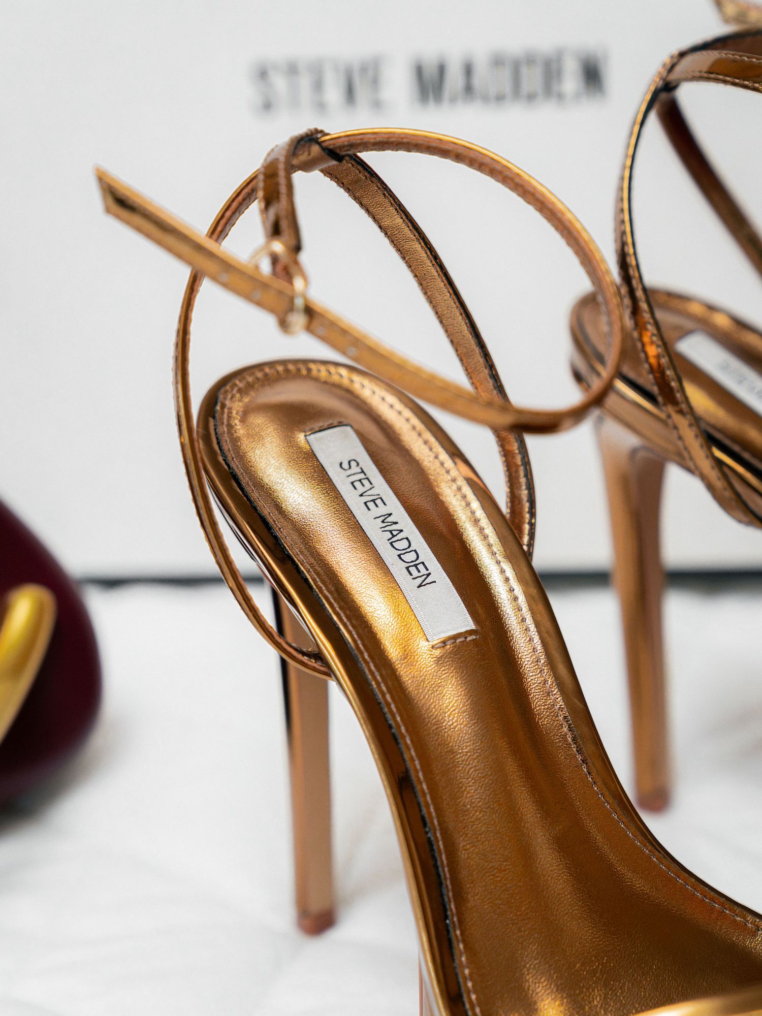 Steve Madden bronze metallic strappy stiletto heels with ankle strap detail on white background.
