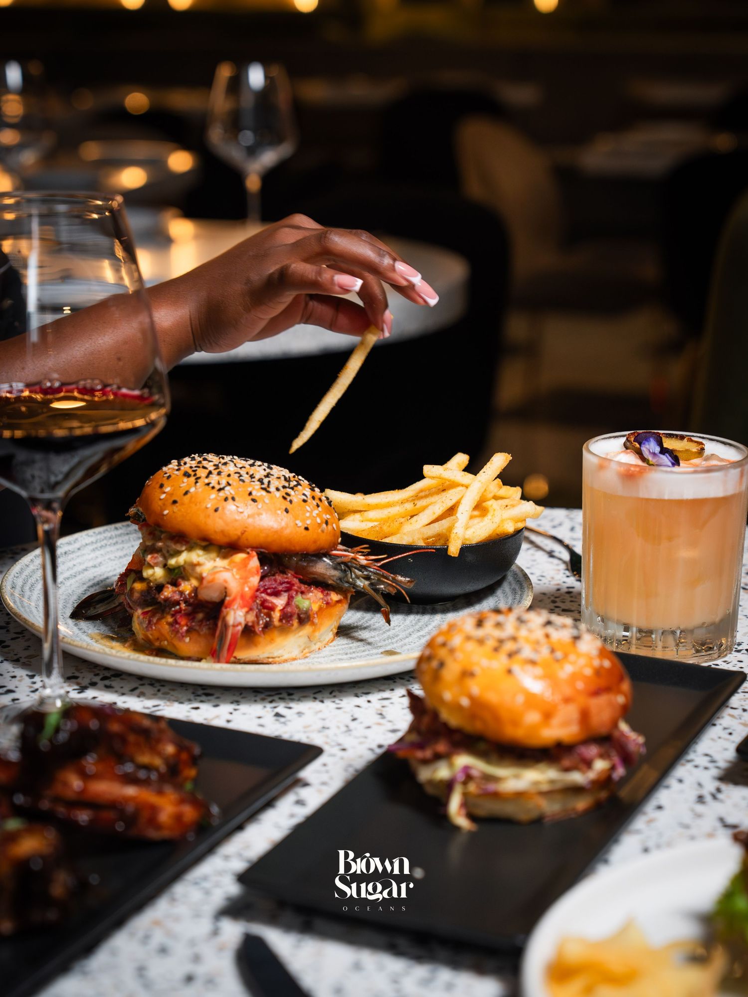 Elegant dining spread at Brown Sugar with burgers, fries, cocktails, and wine on a marble table.