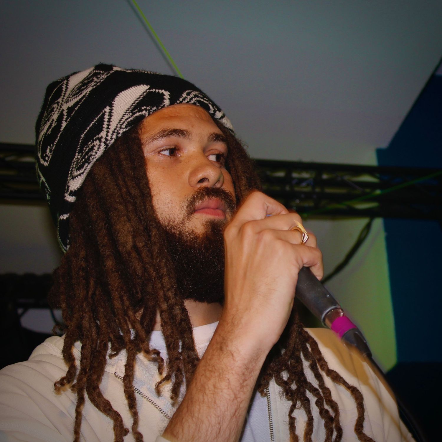 Man with dreadlocks and bandana performing on stage holding a microphone under blue lights.