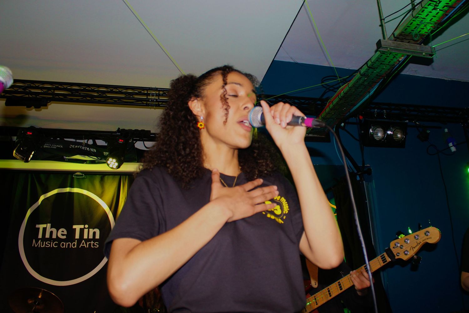 Female singer performing passionately on stage at The Tin Music and Arts venue holding a microphone.