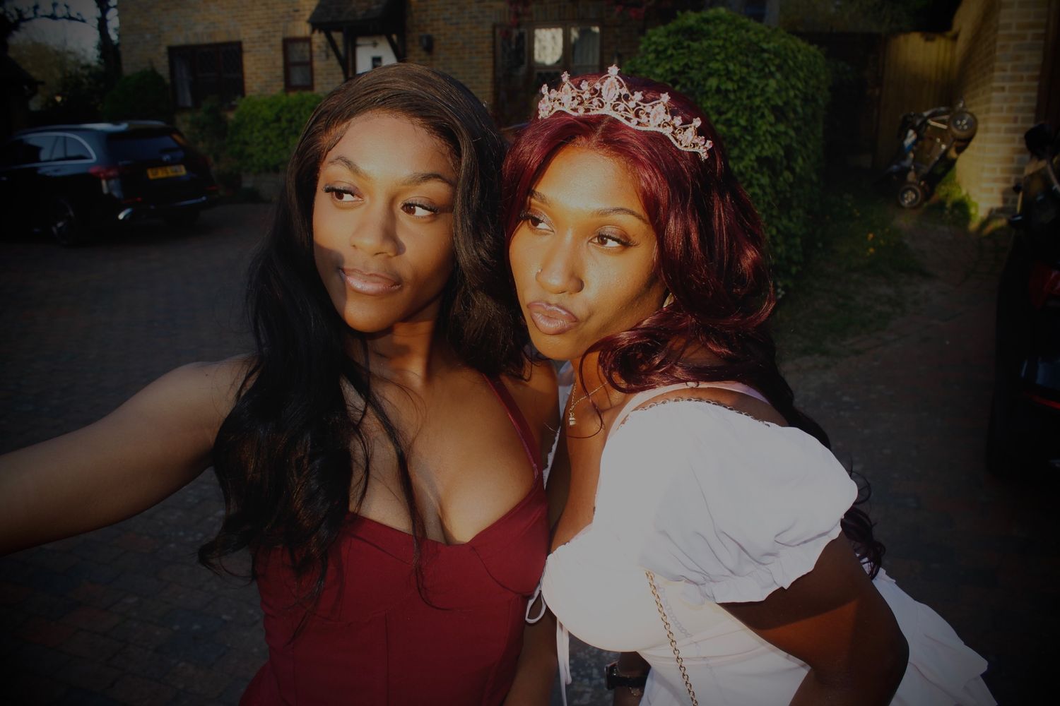 Two young women posing for a selfie outdoors, one wearing a pink tiara and white dress.