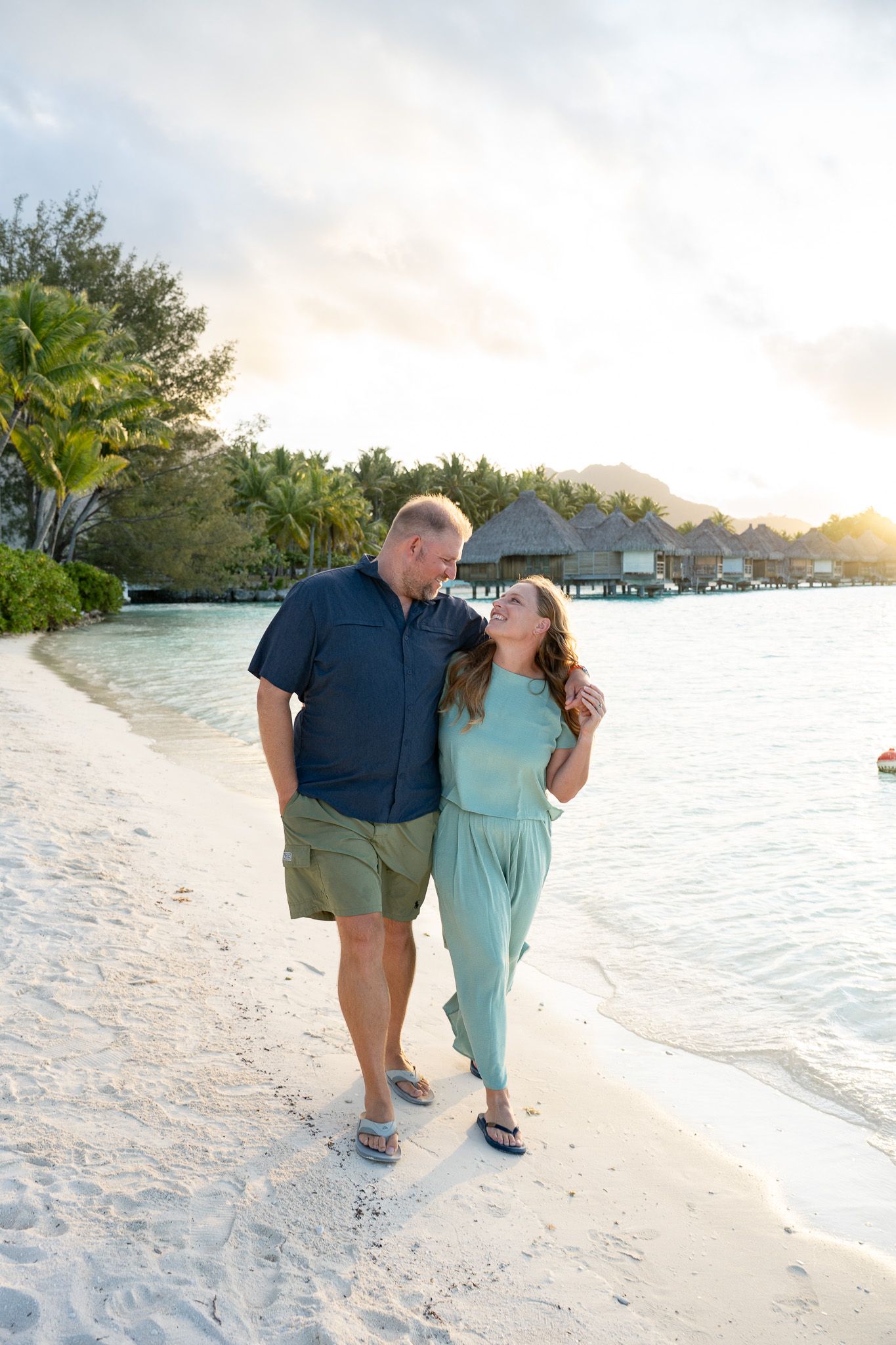Couple walking along a white sand beach during a sunset photoshoot in Bora Bora