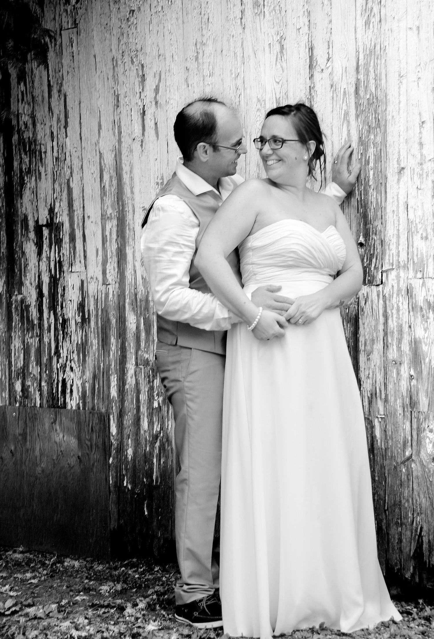 Black and white photo of bride and groom sharing a romantic moment against a rustic wooden wall.