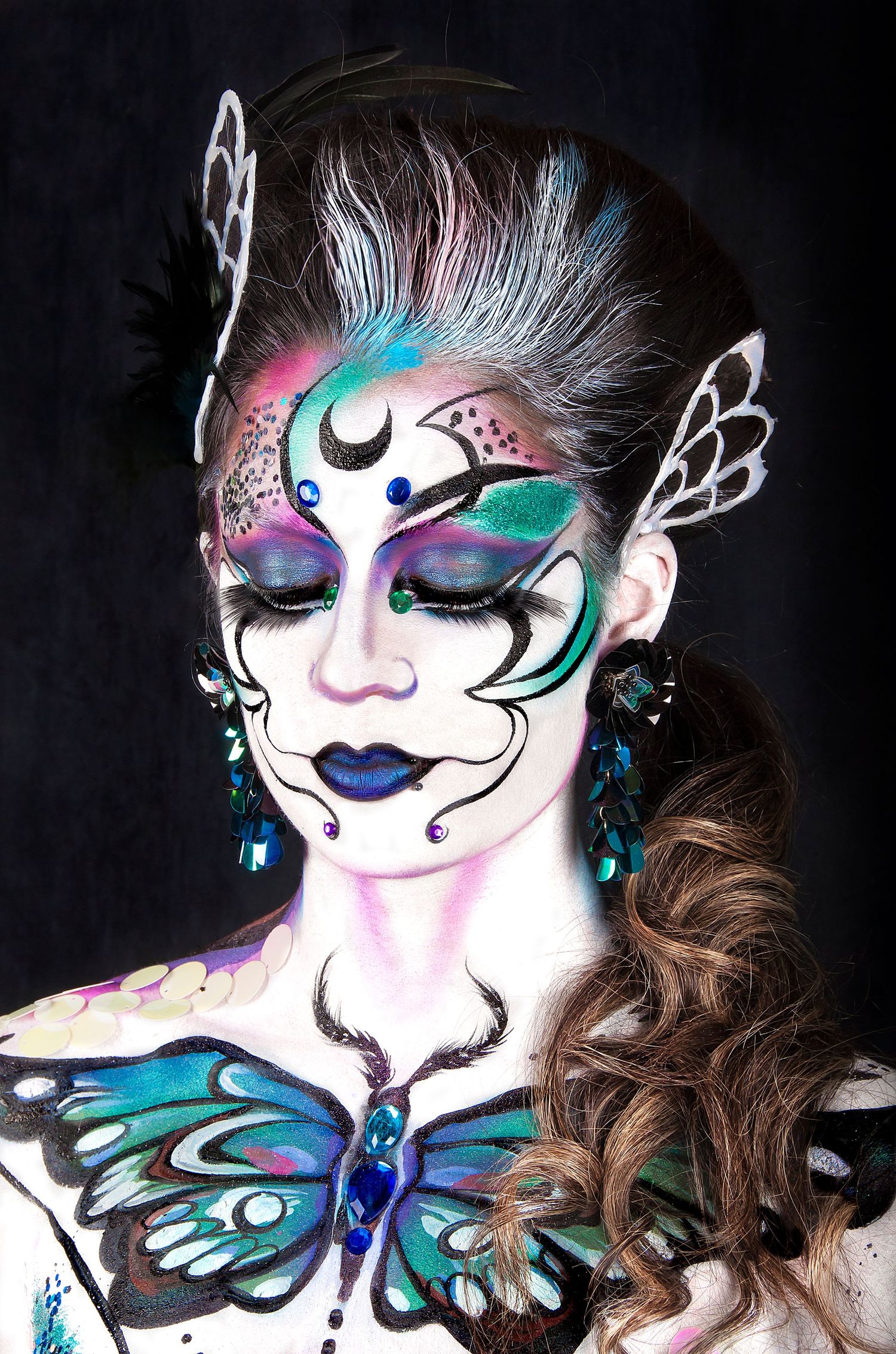 Stunning fantasy butterfly makeup look with teal and purple face paint, crescent moon design, and butterfly chest piece.