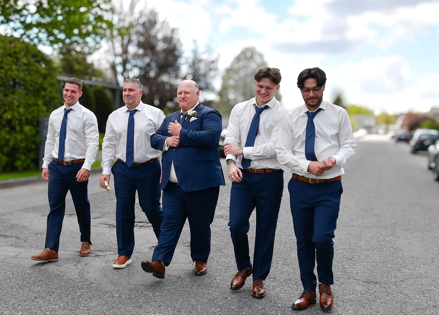 Groom and groomsmen in navy suits and blue ties walking confidently down a street.