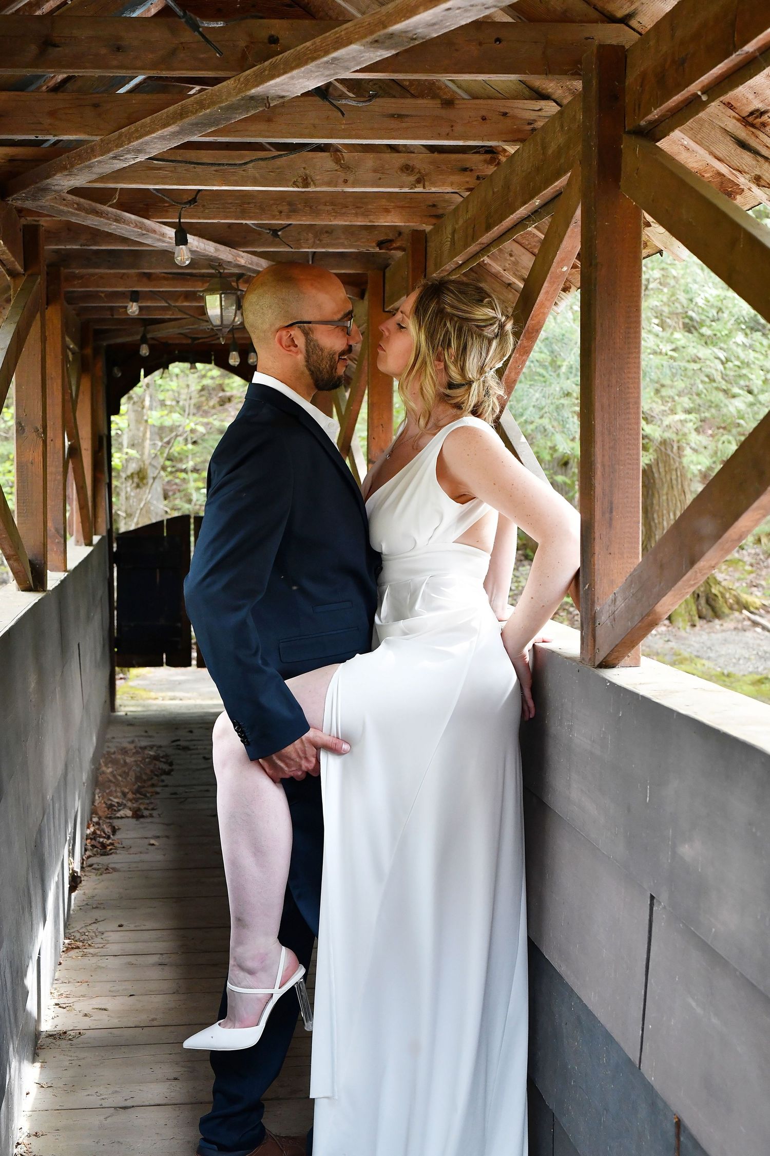 Bride and groom sharing a kiss on a rustic covered wooden bridge during their wedding photo session.