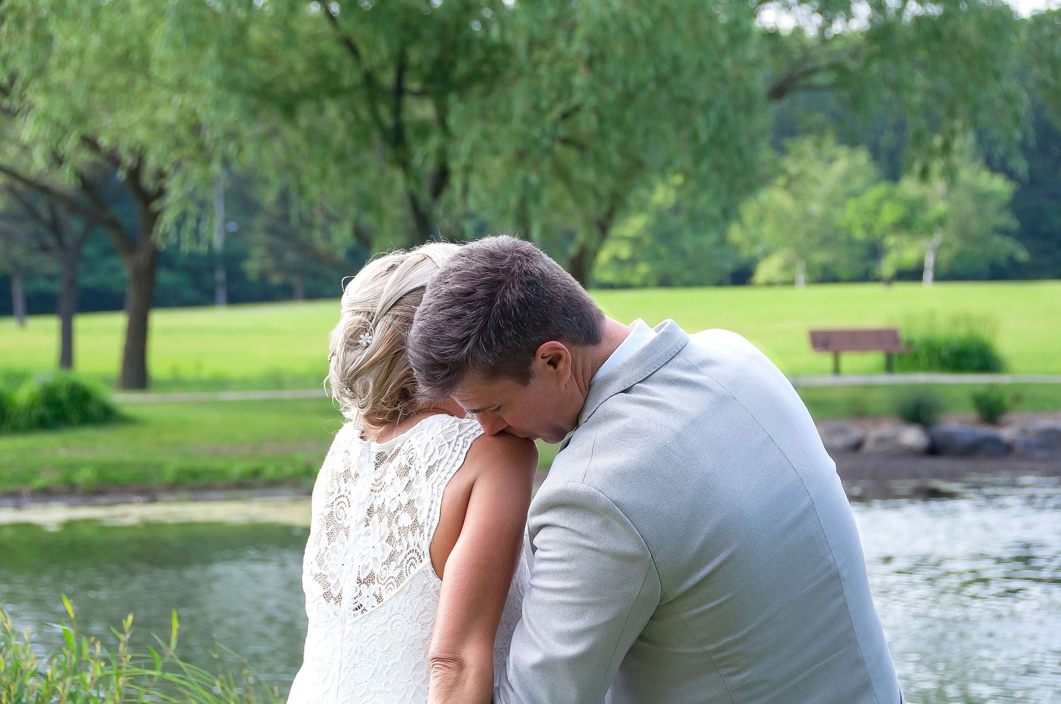 Bride and groom sharing an intimate moment by a pond surrounded by lush greenery.