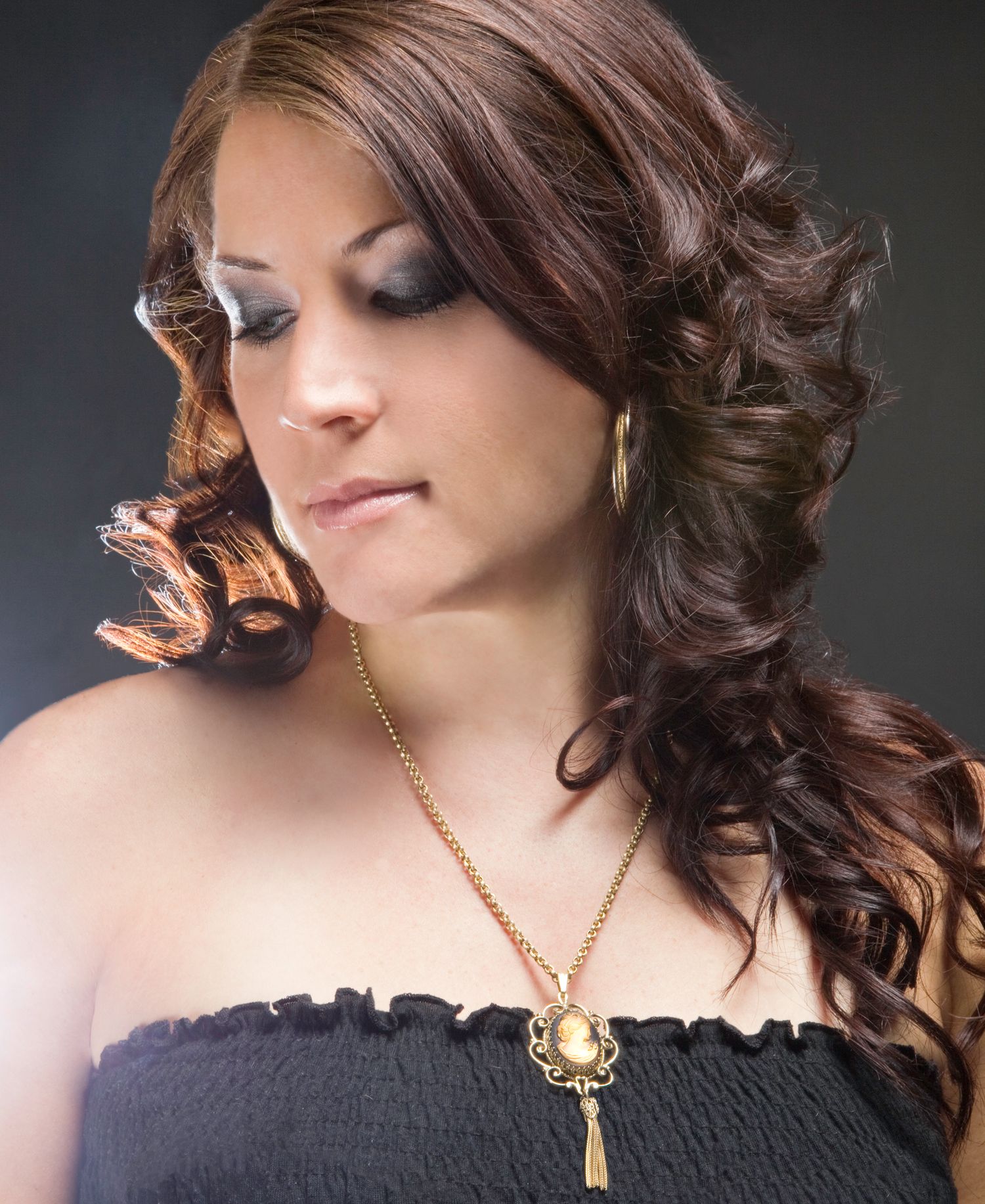 Brunette woman with curly hair wearing black strapless top and vintage cameo necklace.