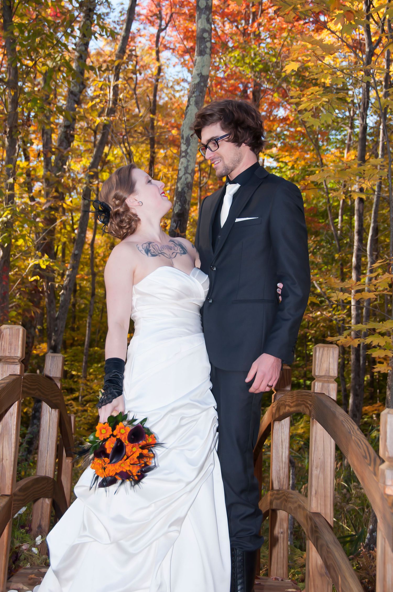 Bride and groom share a romantic gaze on a wooden bridge surrounded by fall foliage.