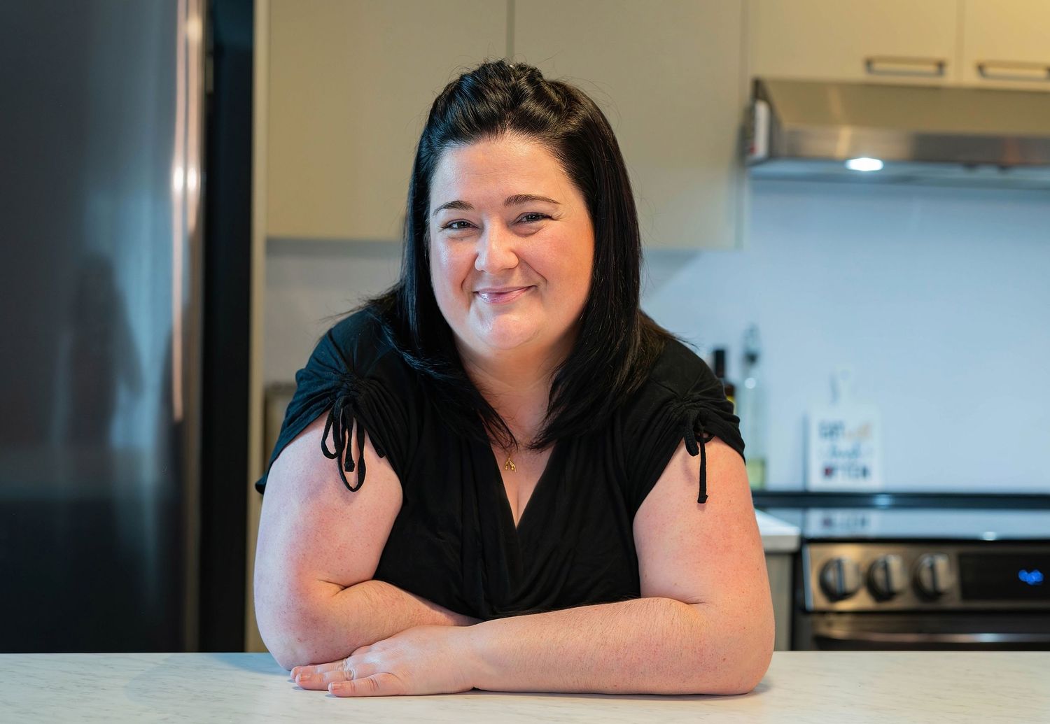 Smiling dark-haired woman leaning on kitchen counter in modern home interior.