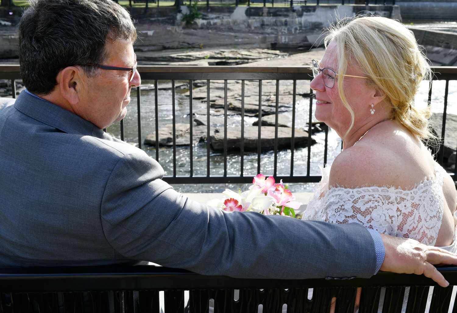 Bride and groom share an intimate moment on a bench near a scenic waterfall on their wedding day.