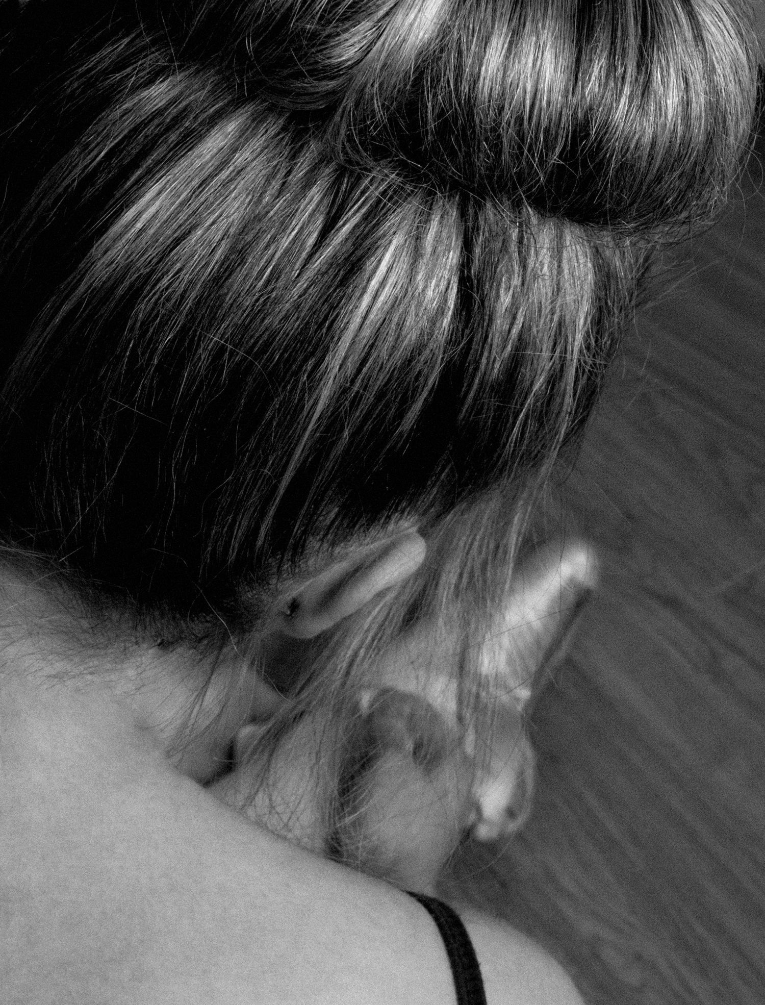 Black and white close-up of a woman with hair in a bun showing a small tattoo behind her ear.