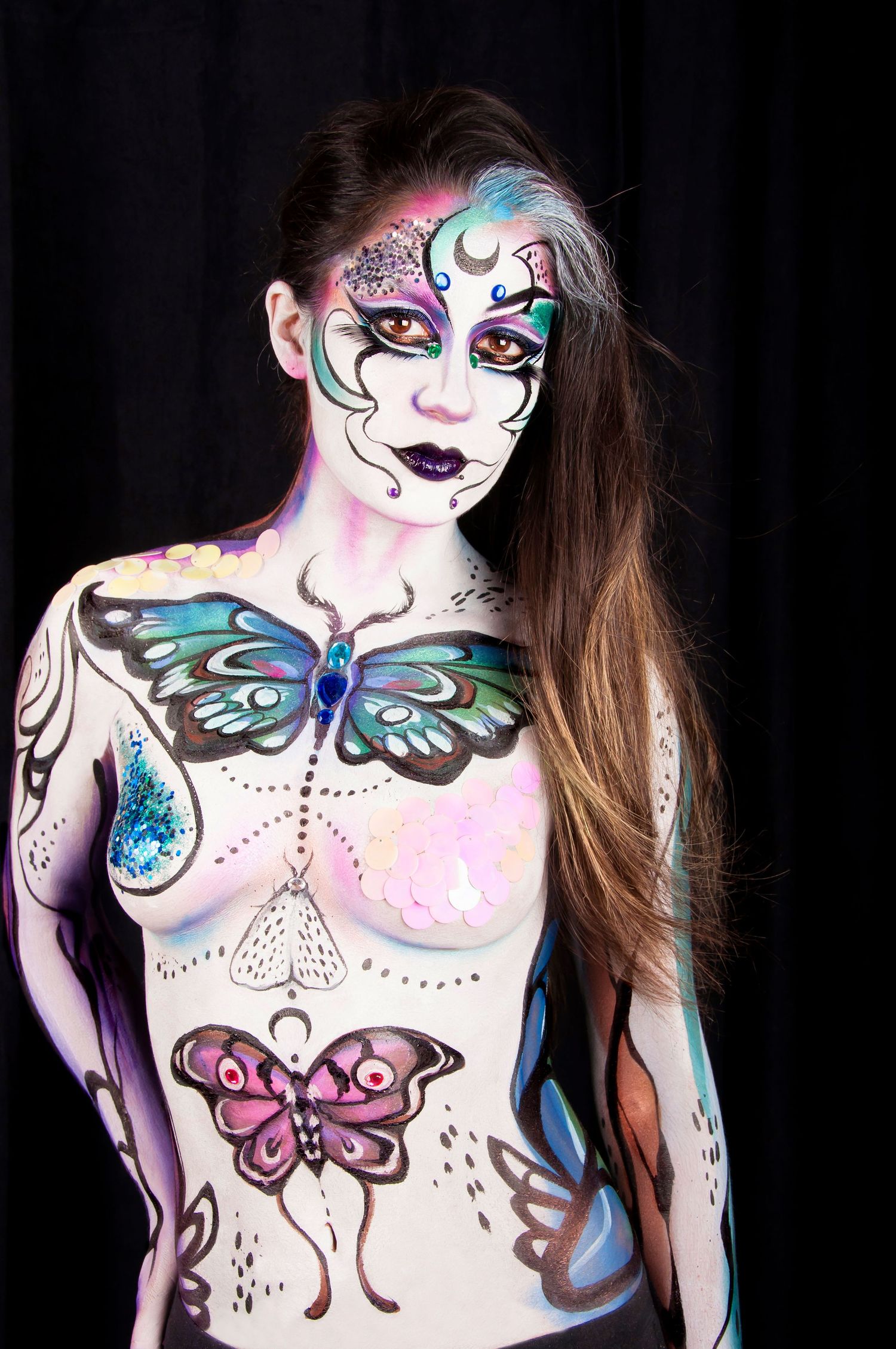 Full body paint art featuring butterfly designs in teal and pink on a woman, dark background.