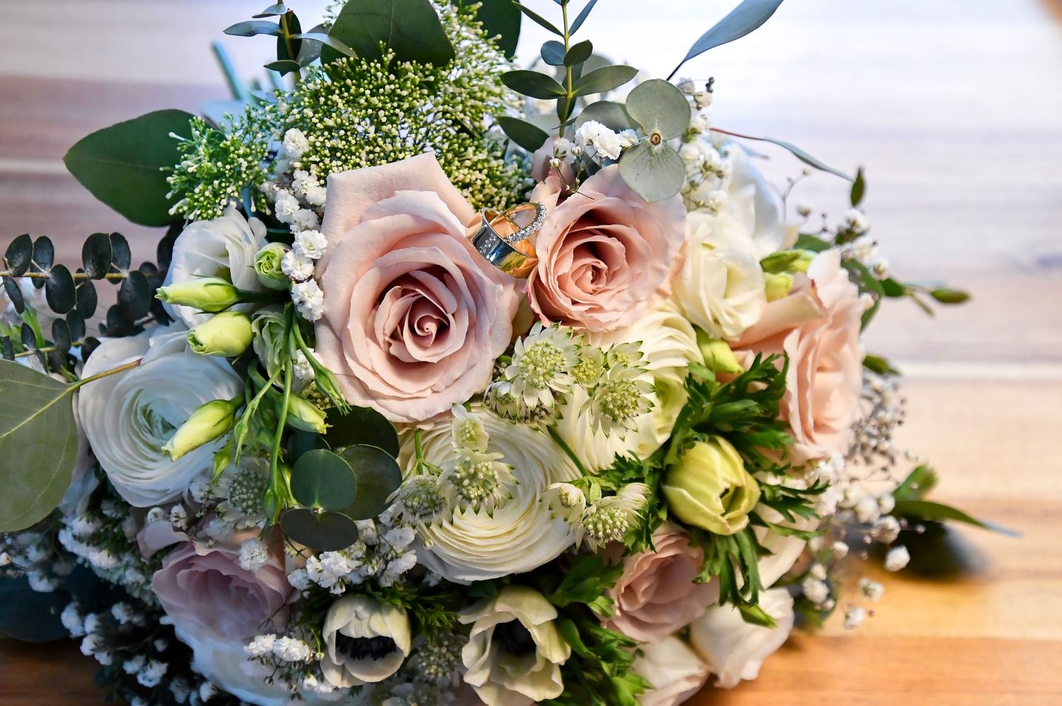 Elegant bridal bouquet of blush roses, white anemones, and greenery on a wooden surface.