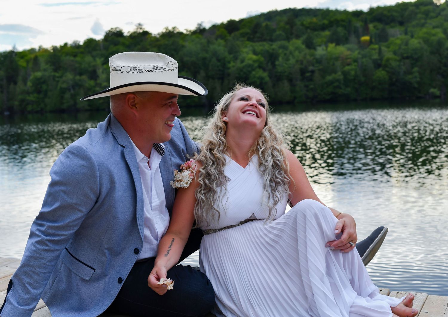Happy couple laughing together on dock by scenic lake surrounded by green hills.