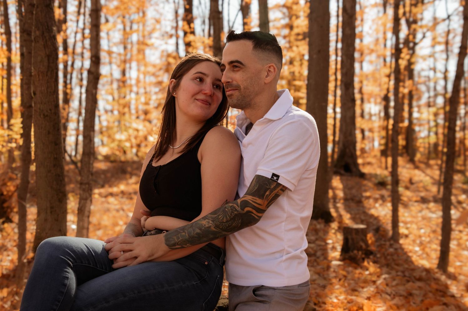 Romantic couple embracing in a golden autumn forest during an engagement photo session.