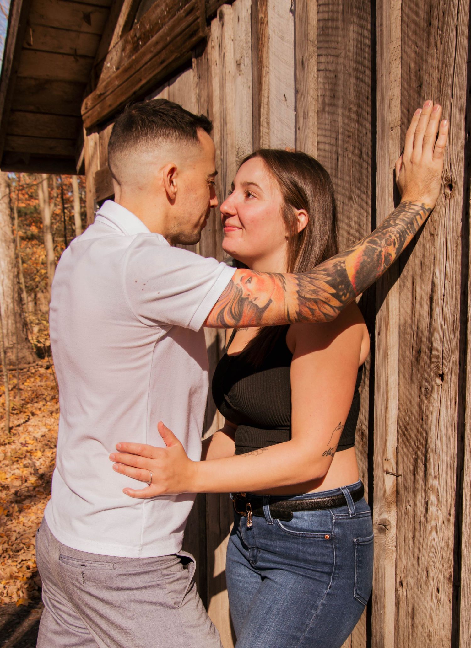 Couple sharing romantic moment leaning against rustic wooden barn wall in autumn setting.