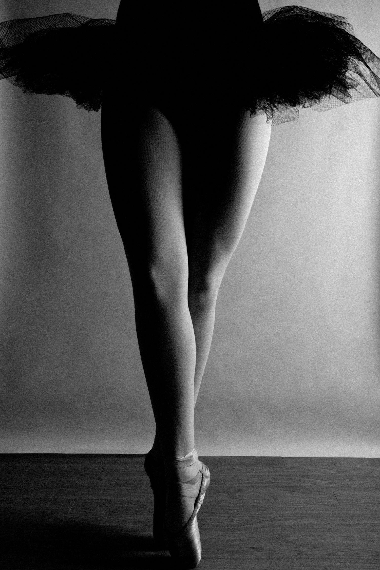 Ballerina in black tutu standing en pointe in black and white studio photo.