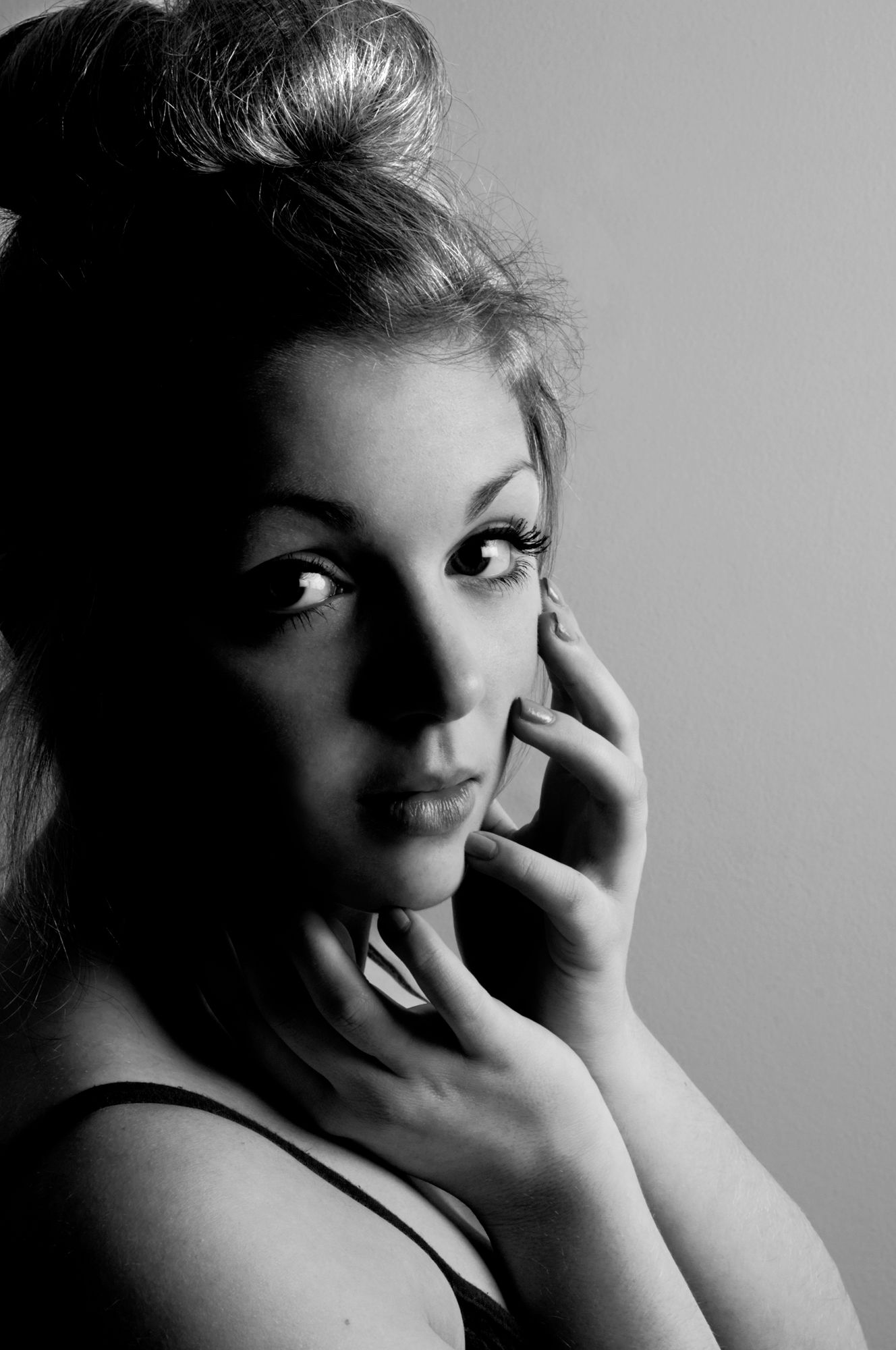 Black and white portrait of woman with updo hairstyle posing with hand near her face.