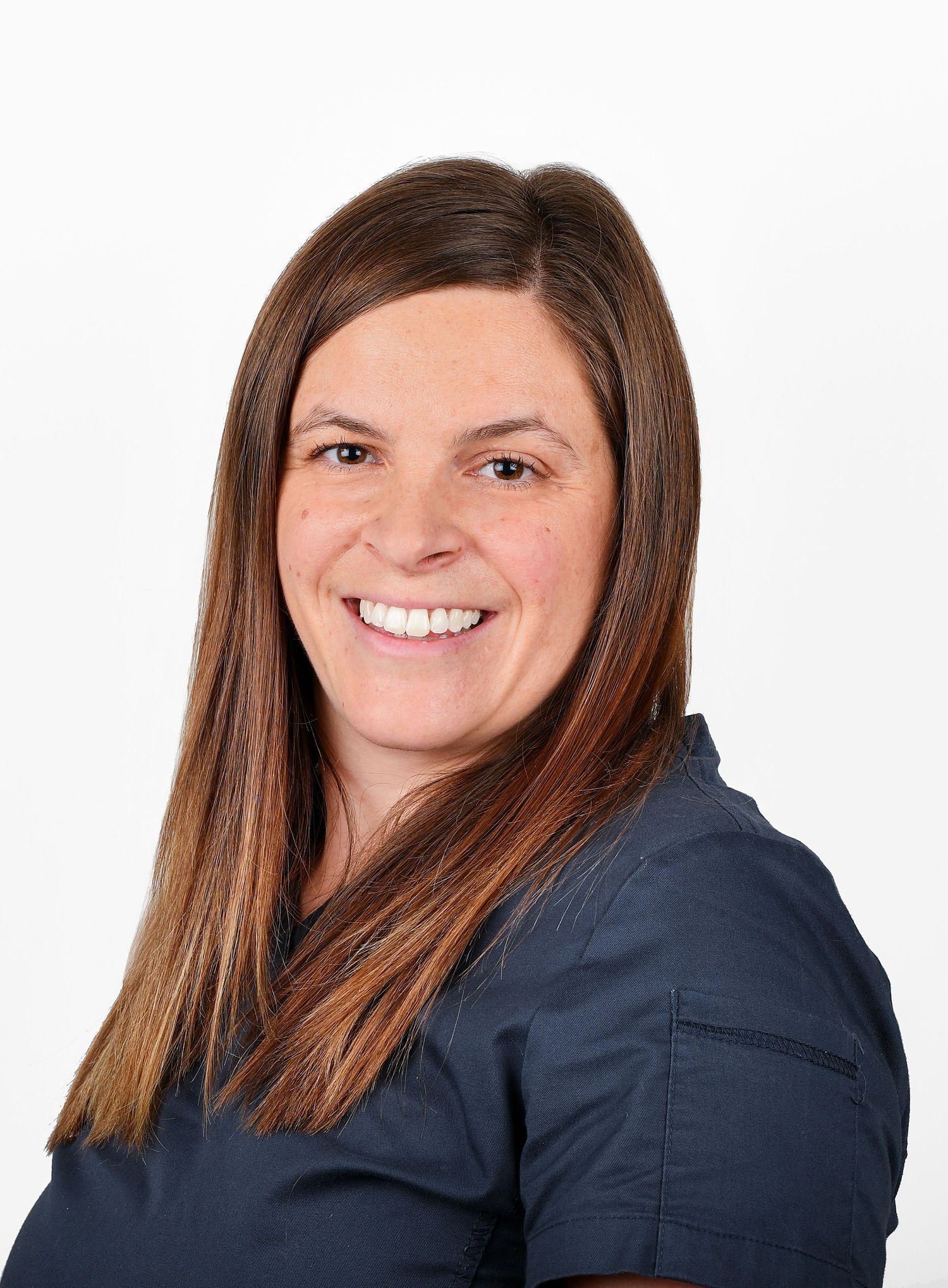 Professional woman in navy scrubs with long brown hair smiling against a white background.