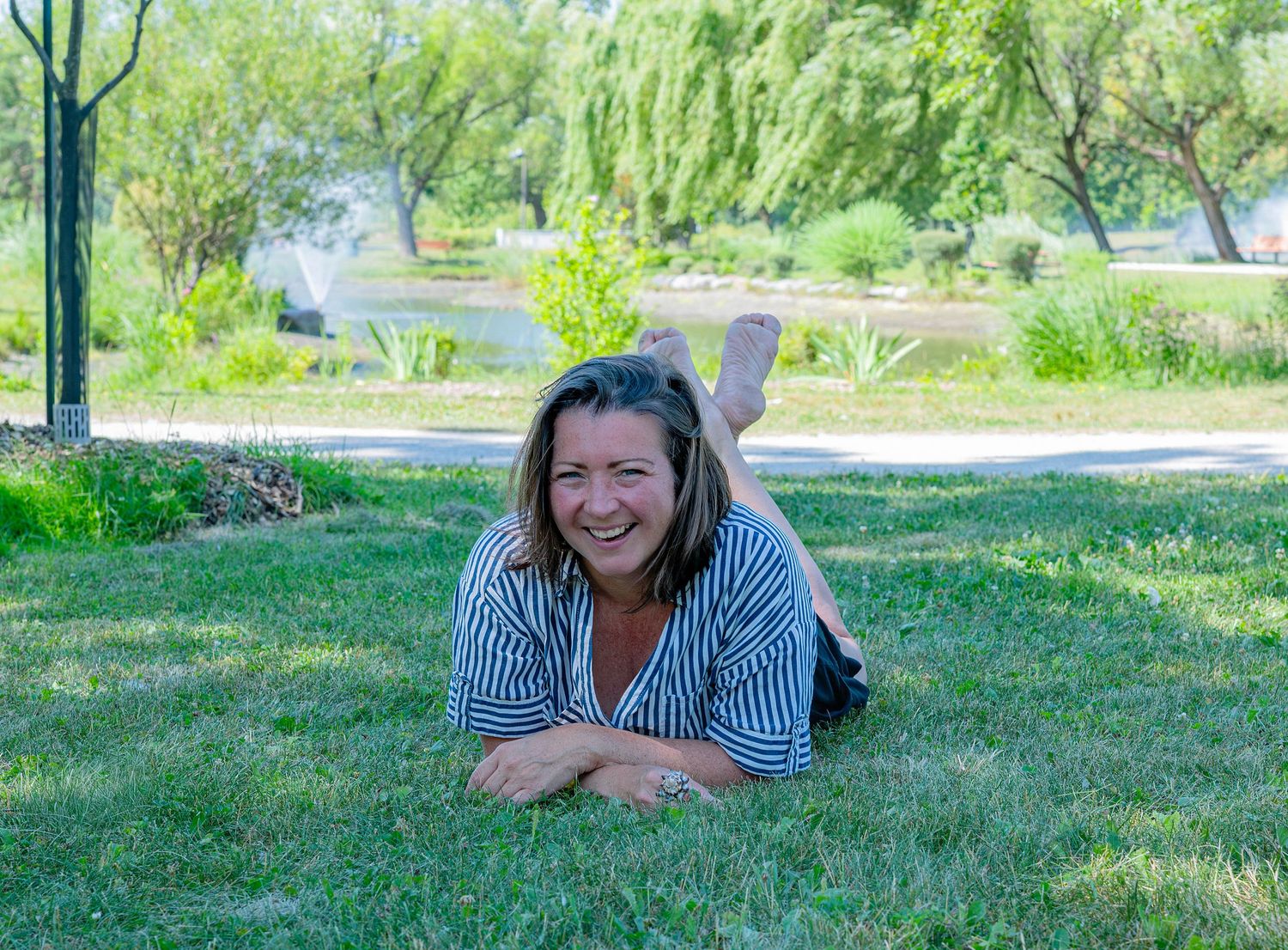 Smiling middle-aged woman lying on green grass in sunny park setting.