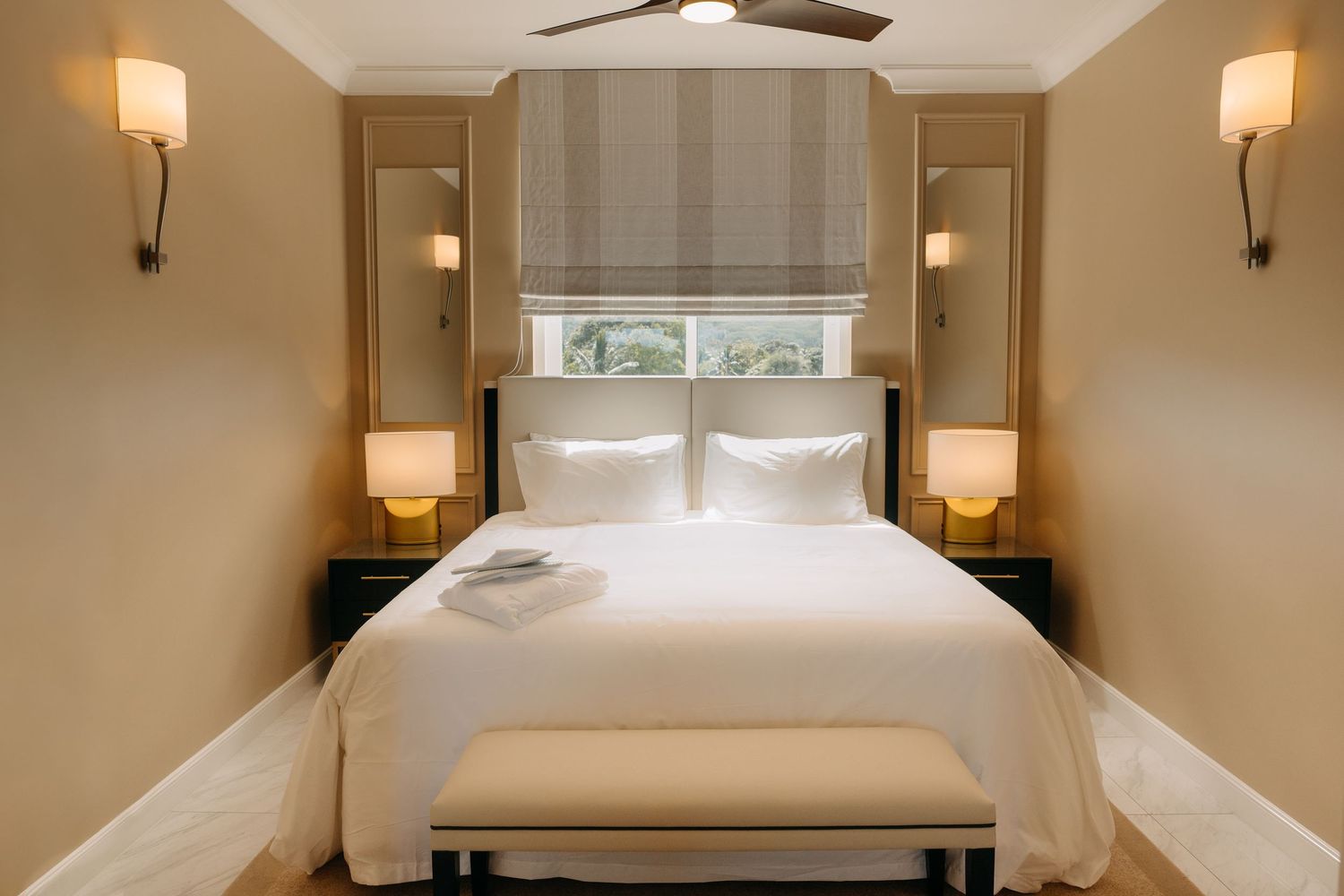 Elegant hotel bedroom with white bedding, warm lighting, wood paneling, and a bench at the foot of the bed.