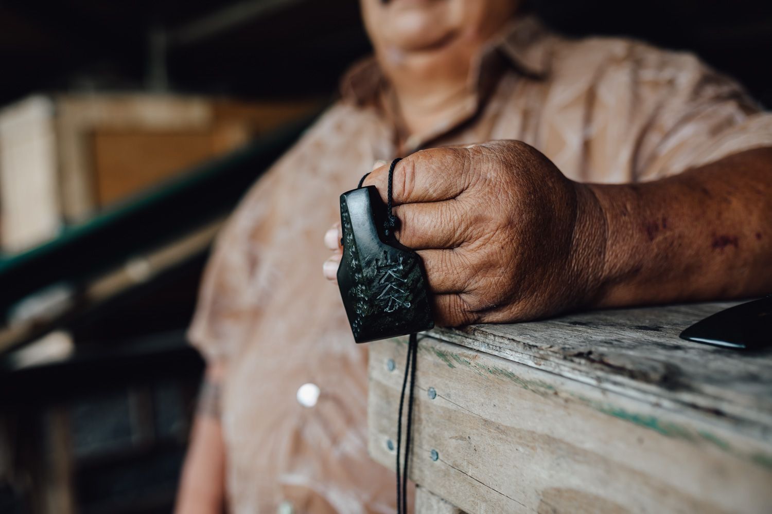 Close-up of weathered hands holding a small black tool against a wooden surface.