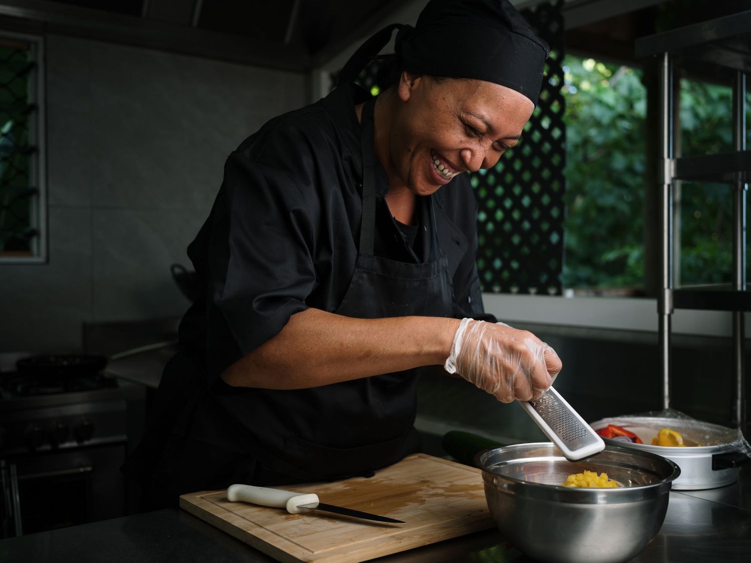 Smiling chef in black uniform preparing colorful ingredients in a metal bowl in a professional kitchen.