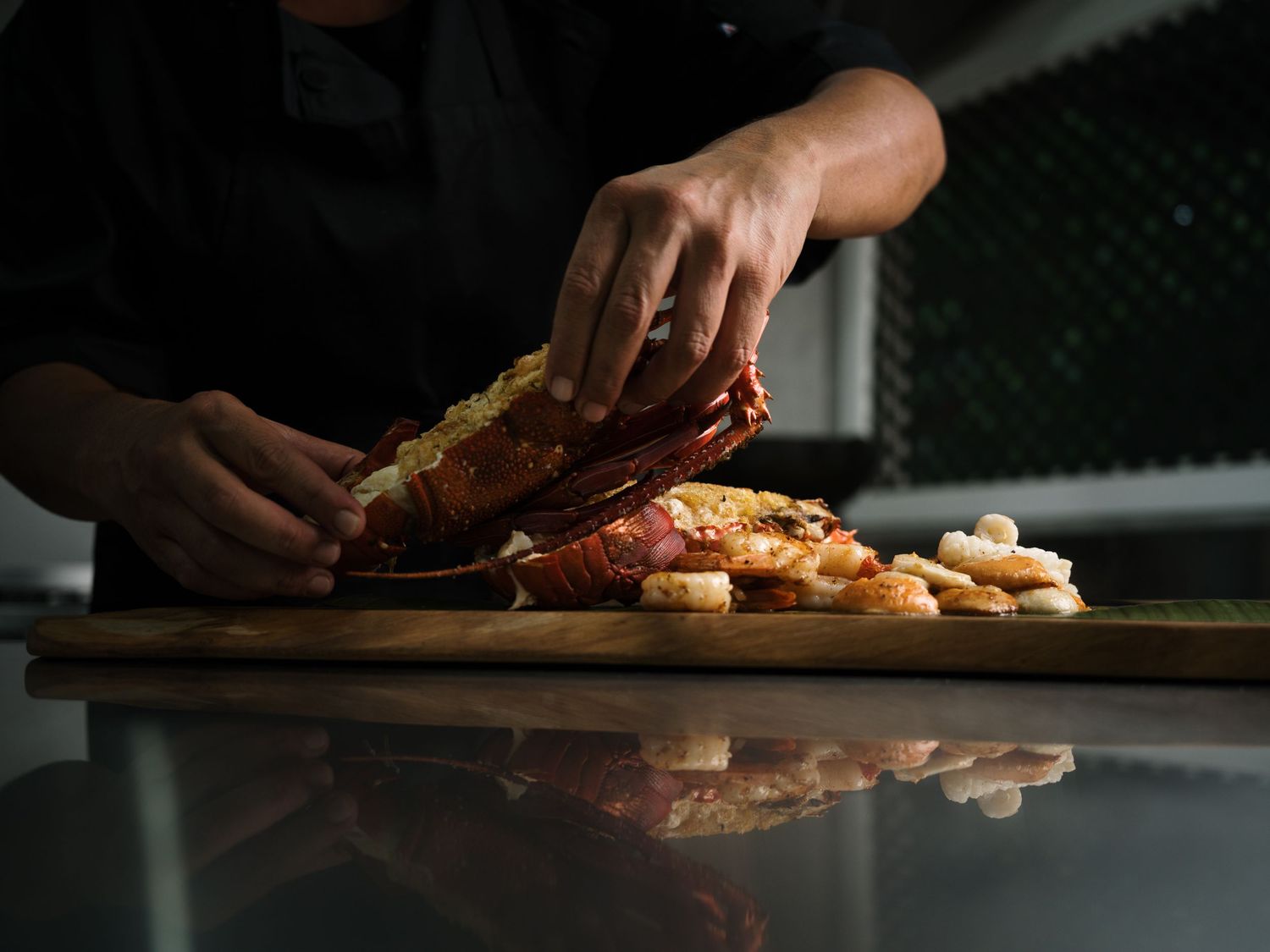 Chef preparing a fresh lobster dish with shrimp on a wooden cutting board in a professional kitchen.