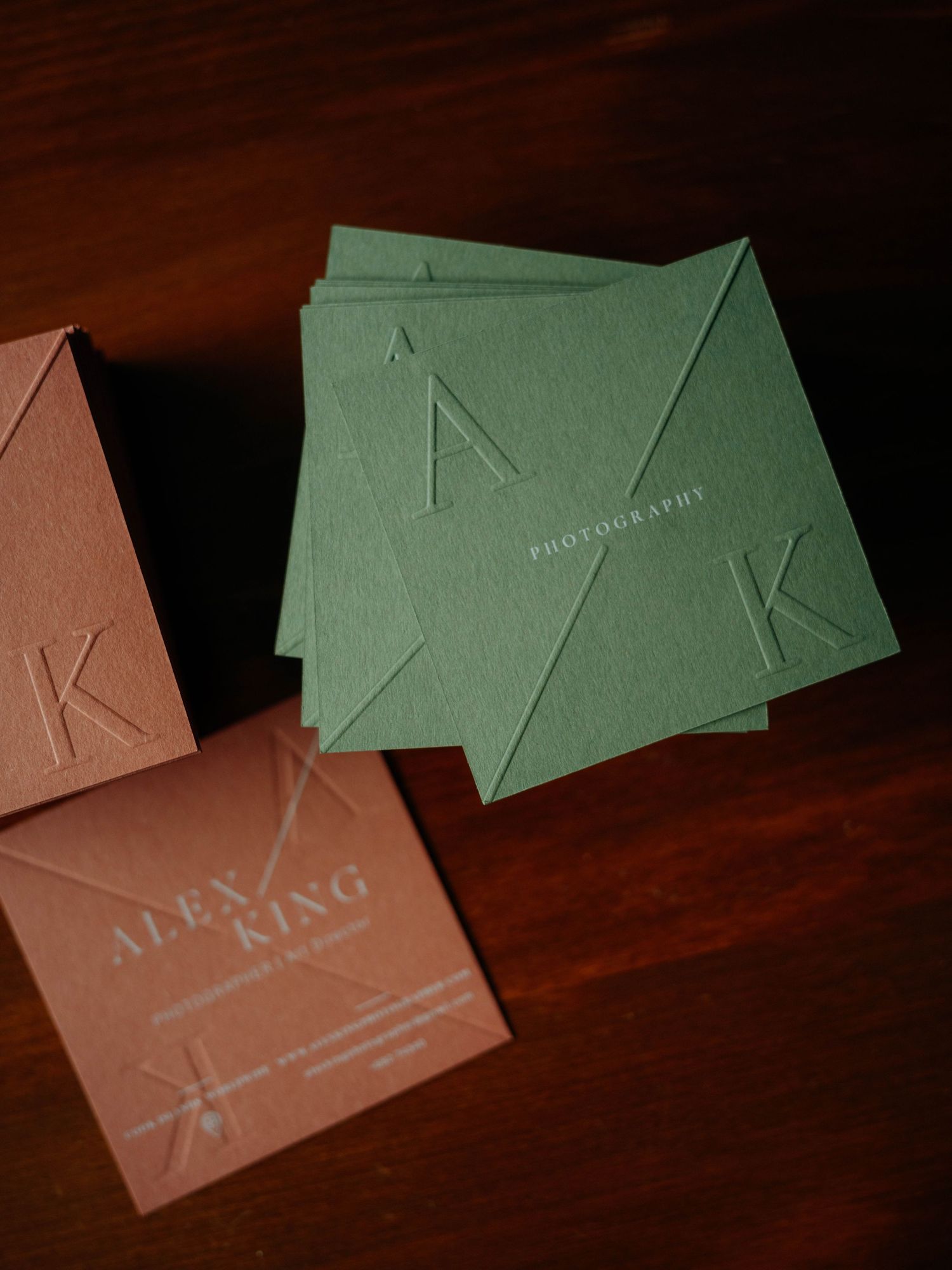 Green and pink letterpress business cards for Alex King Photography displayed on a wooden surface.