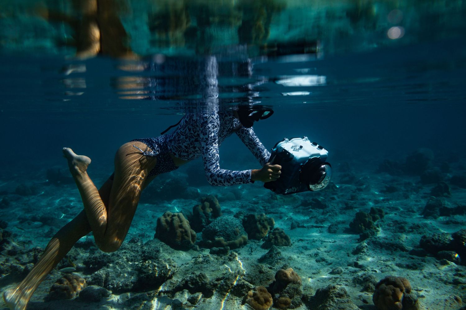 Underwater shot of freediver swimming above coral reef in clear turquoise tropical ocean water.