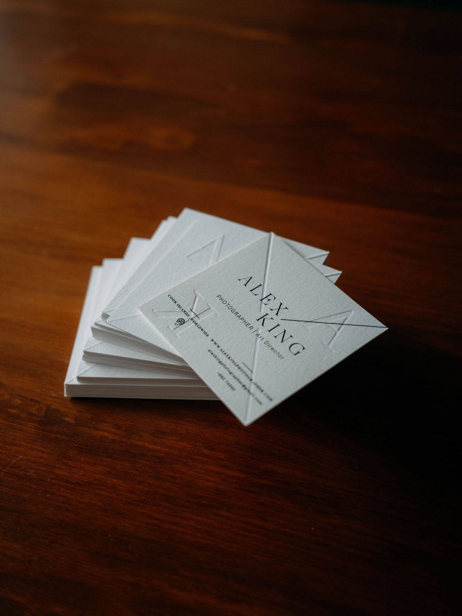 Stack of white business cards for Alex King photographer displayed on a wooden table.