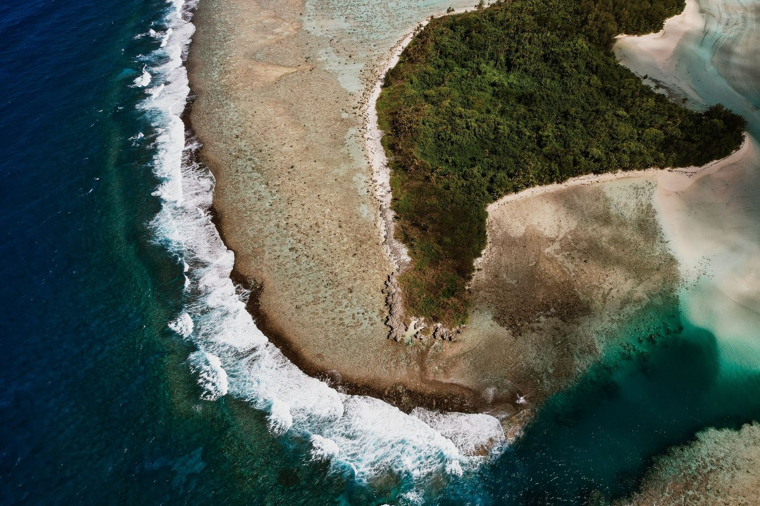 Aerial view of a tropical island with lush green vegetation, sandy shores, and turquoise ocean waves crashing on coral reefs.