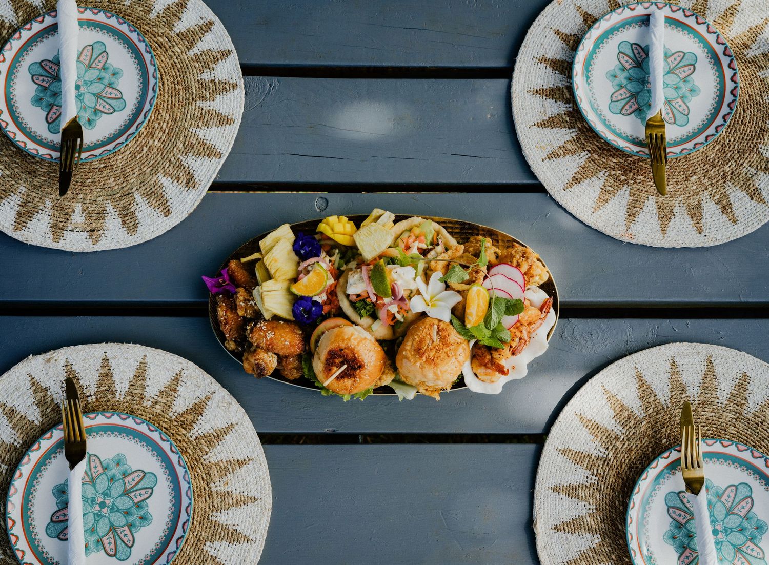 Elegant table setting with gold charger plates, blue flatware, and a centerpiece platter of gourmet seafood appetizers.