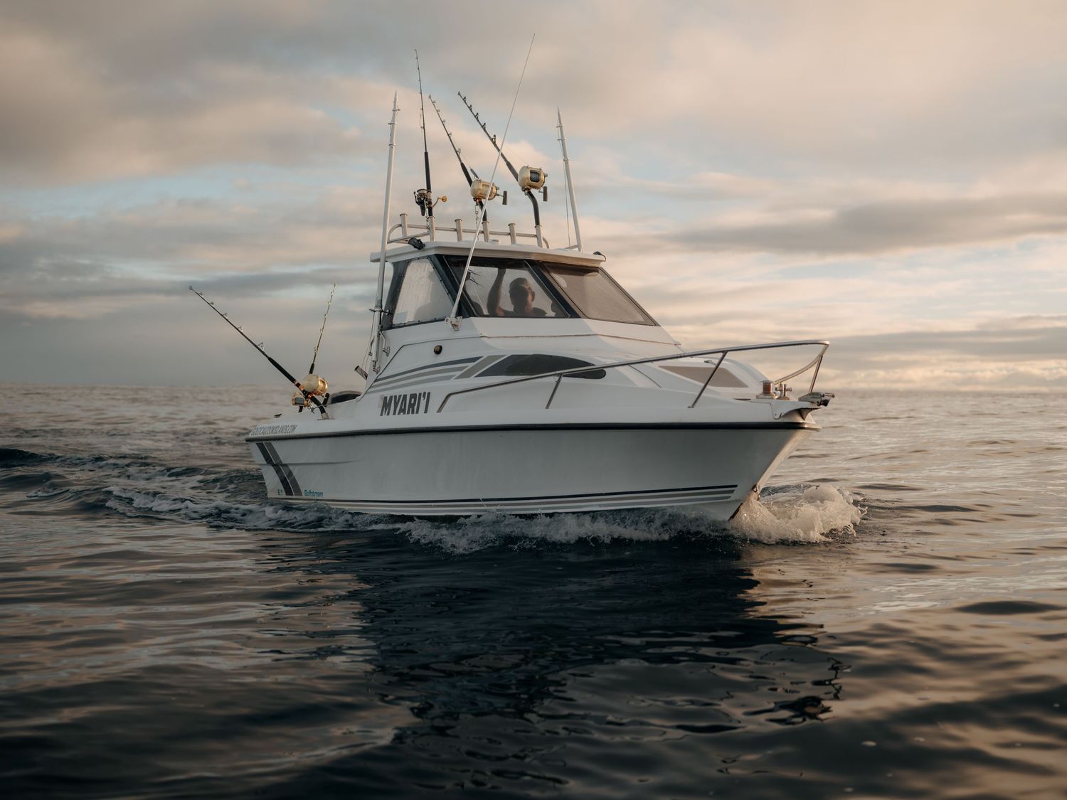 A sport fishing boat named Wygant navigates open ocean waters under a dramatic cloudy sky at dusk.