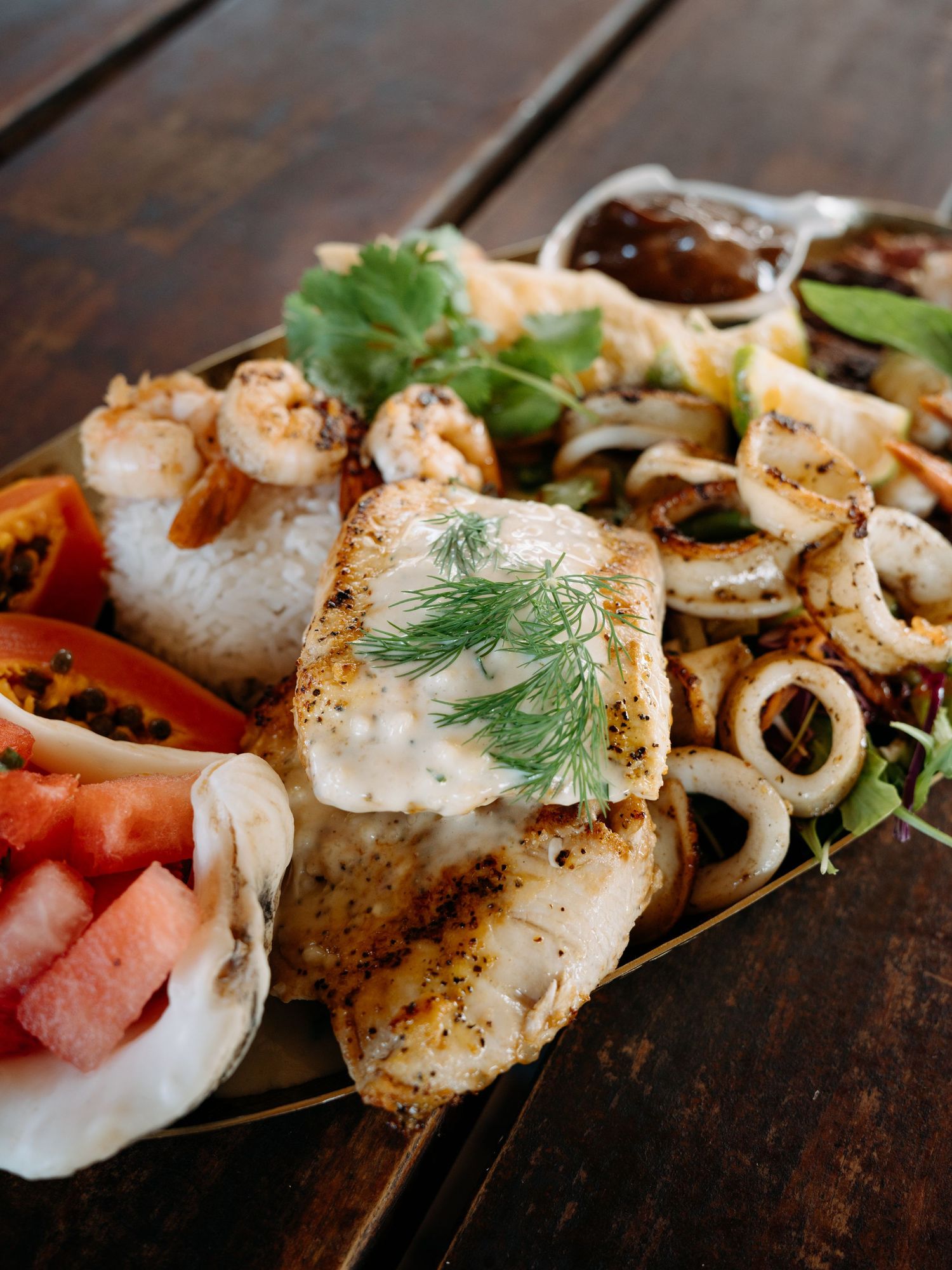 Grilled seafood platter with fish, shrimp, calamari, rice, tomatoes, and fresh herbs on a rustic wooden table.