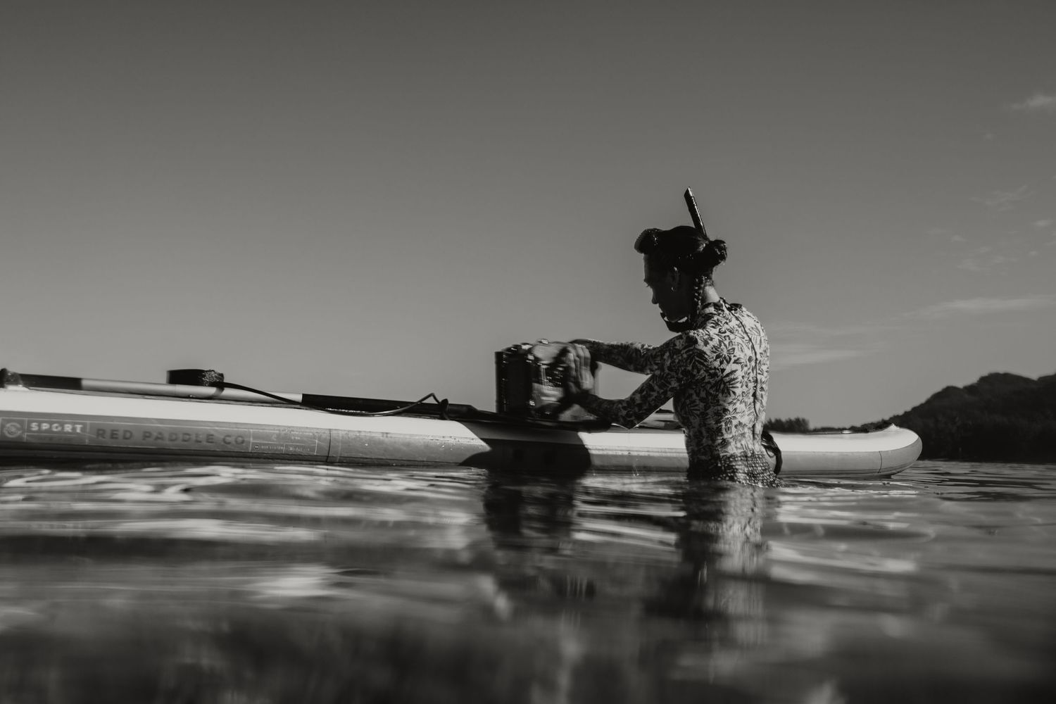 Silhouette of person on paddleboard in calm ocean water against clear sky in black and white.