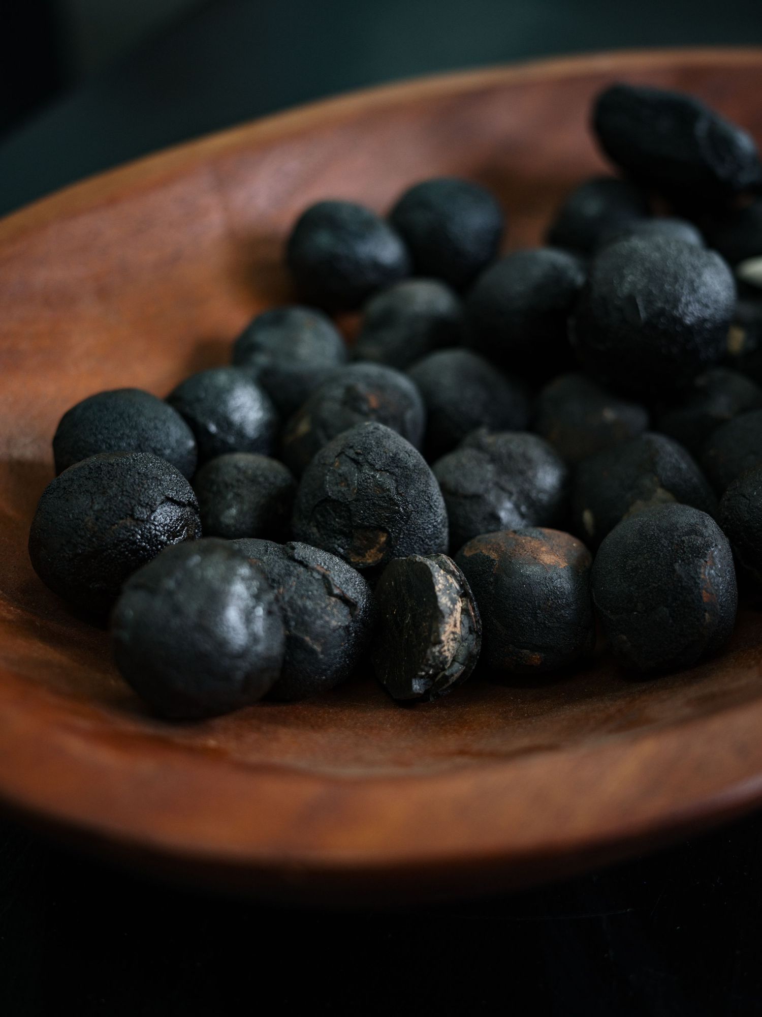 Dark black dried berries piled in a rustic wooden bowl, perfect for culinary or herbal use.