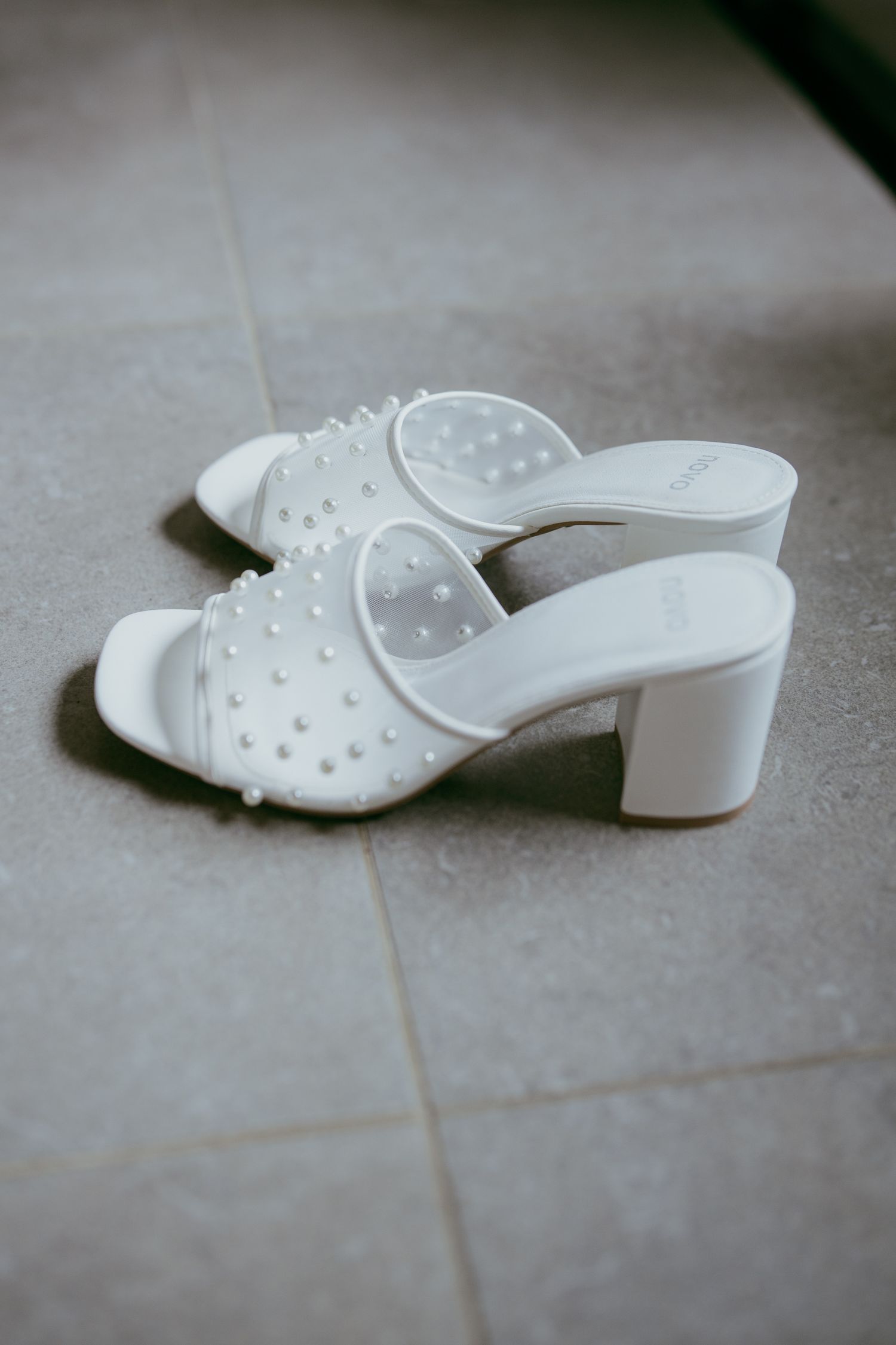 White studded block heel mule sandals on gray tile floor.