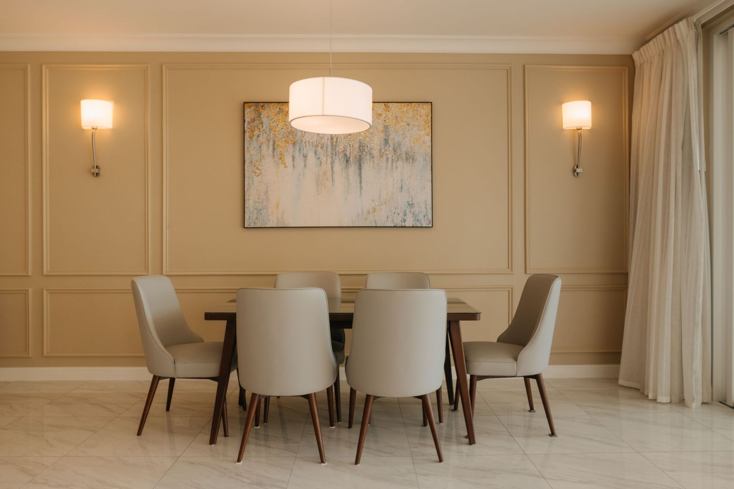 Elegant dining room with beige wainscoting, drum pendant light, upholstered chairs, dark wood table, and abstract wall art.