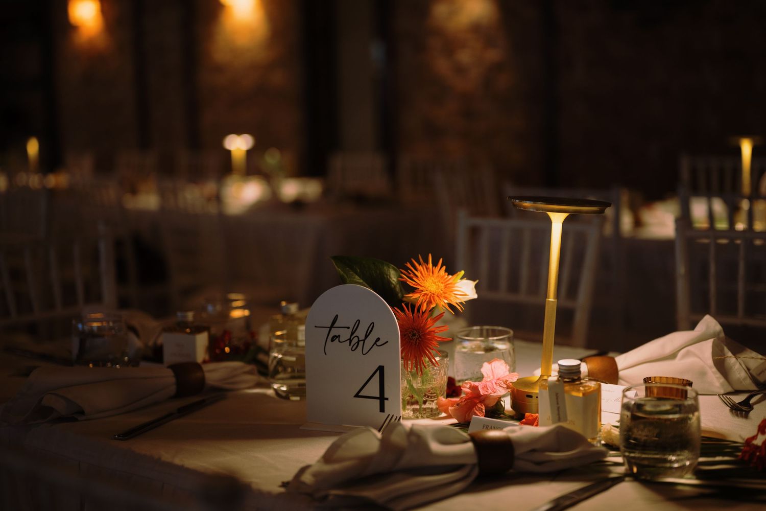Elegant wedding reception table with floral centerpiece, table number 4 sign, candles, and warm ambient lighting.