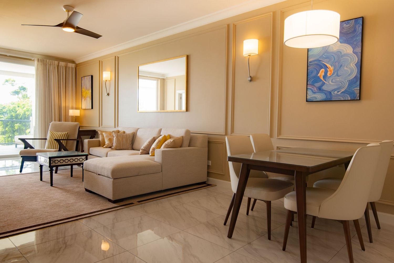 Elegant hotel suite with beige sectional sofa, glass dining table, marble floors, and balcony access.