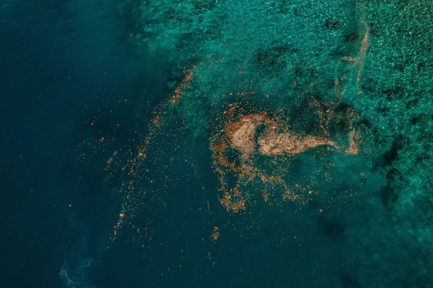 Aerial view of vibrant teal ocean water with scattered golden coral reef formations visible beneath the surface.