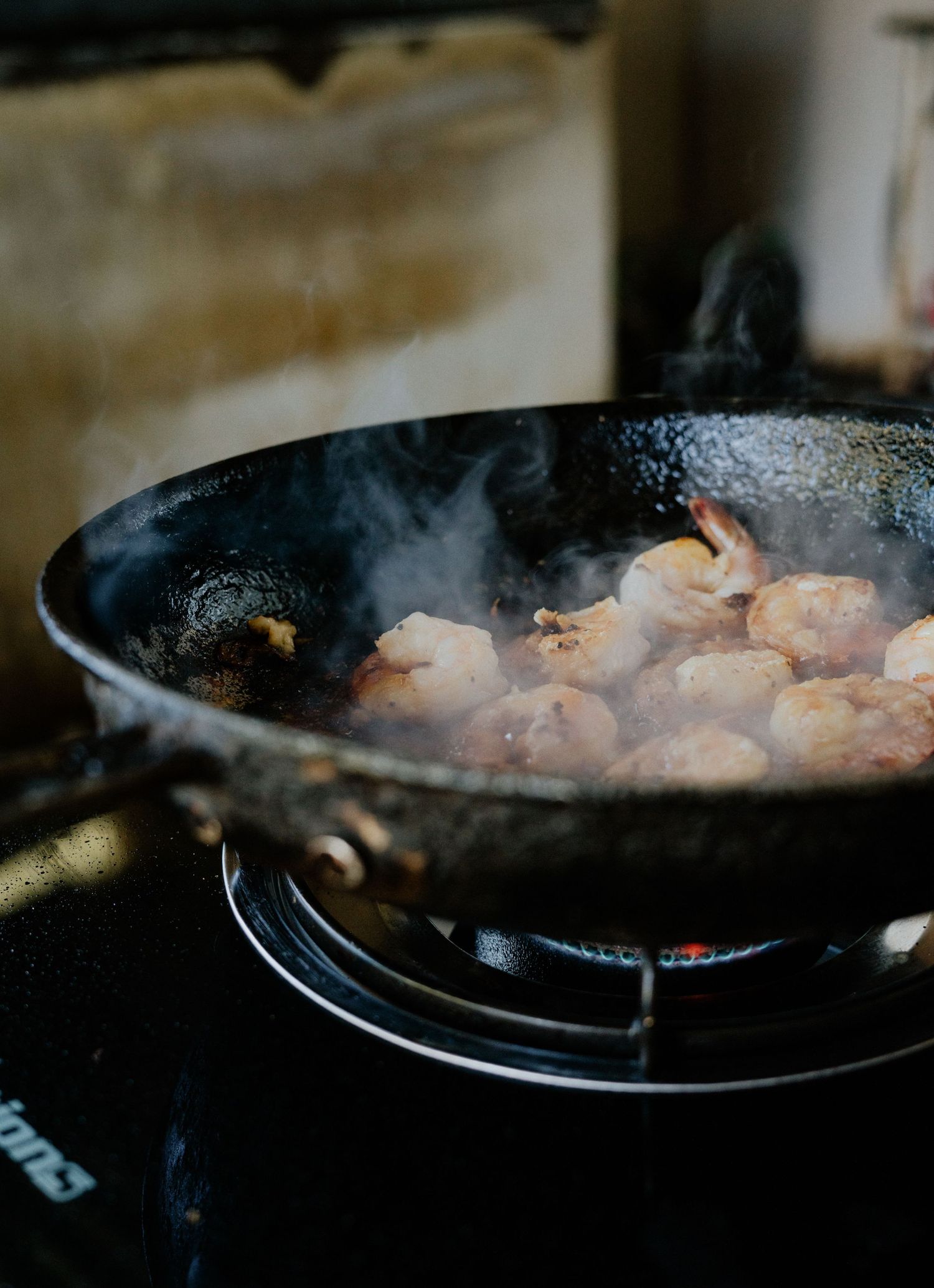 Shrimp sizzling in a black wok on a gas stove, with steam rising in a rustic kitchen setting.
