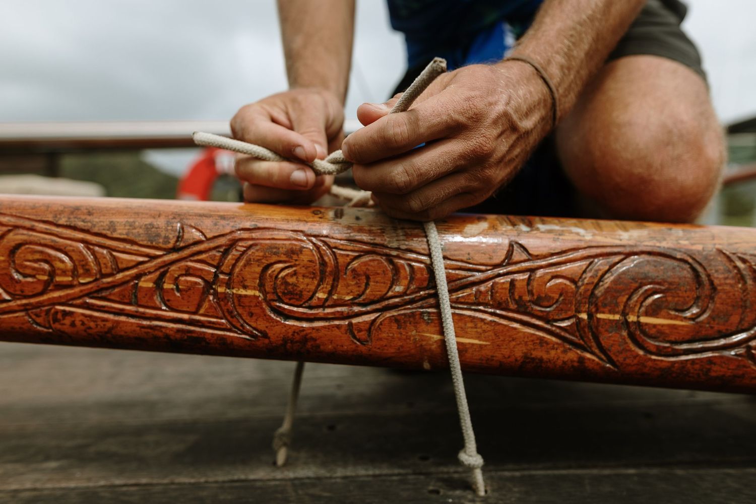 Close-up of hands carving intricate Maori patterns into a wooden canoe using traditional tools.