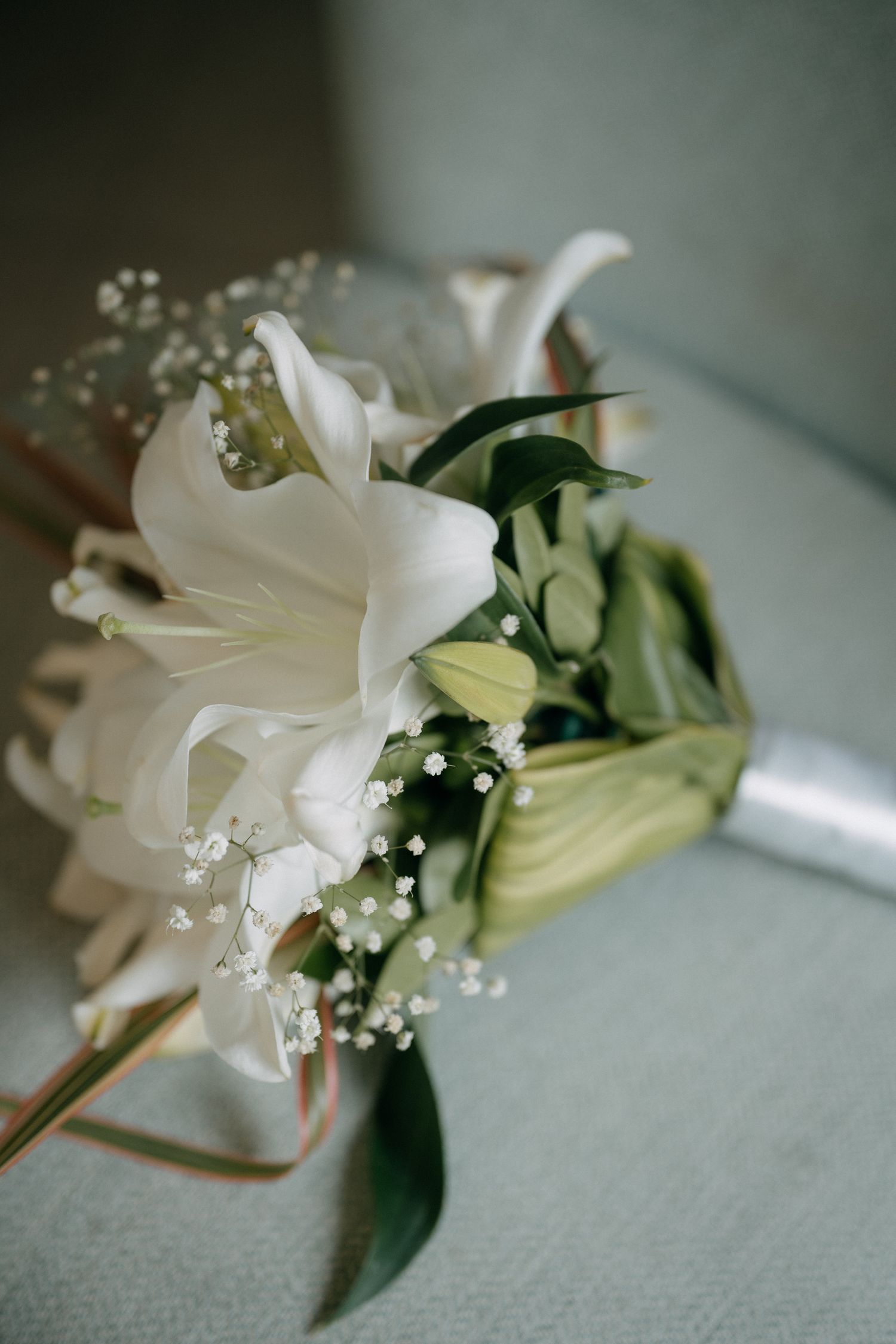 Elegant bridal bouquet with white lilies, calla lilies, and baby's breath accented with green leaves and satin ribbon.