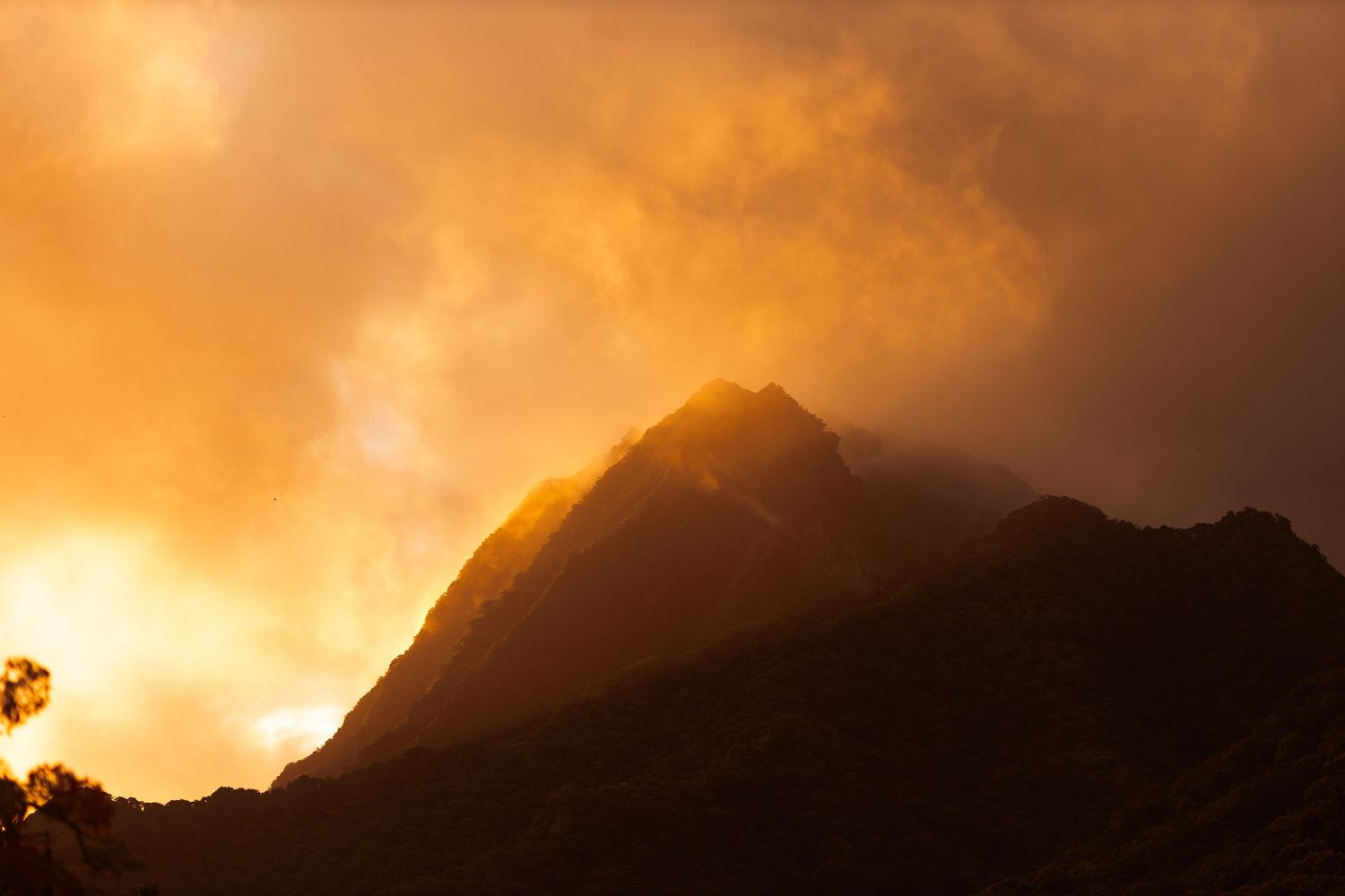 Golden sunset illuminates dramatic mountain peak shrouded in glowing clouds against a fiery orange sky.