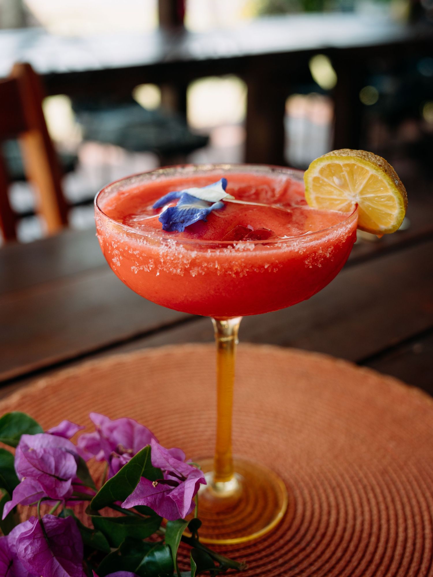 Vibrant red frozen strawberry margarita garnished with lemon slice and blue flower on salted rim glass.